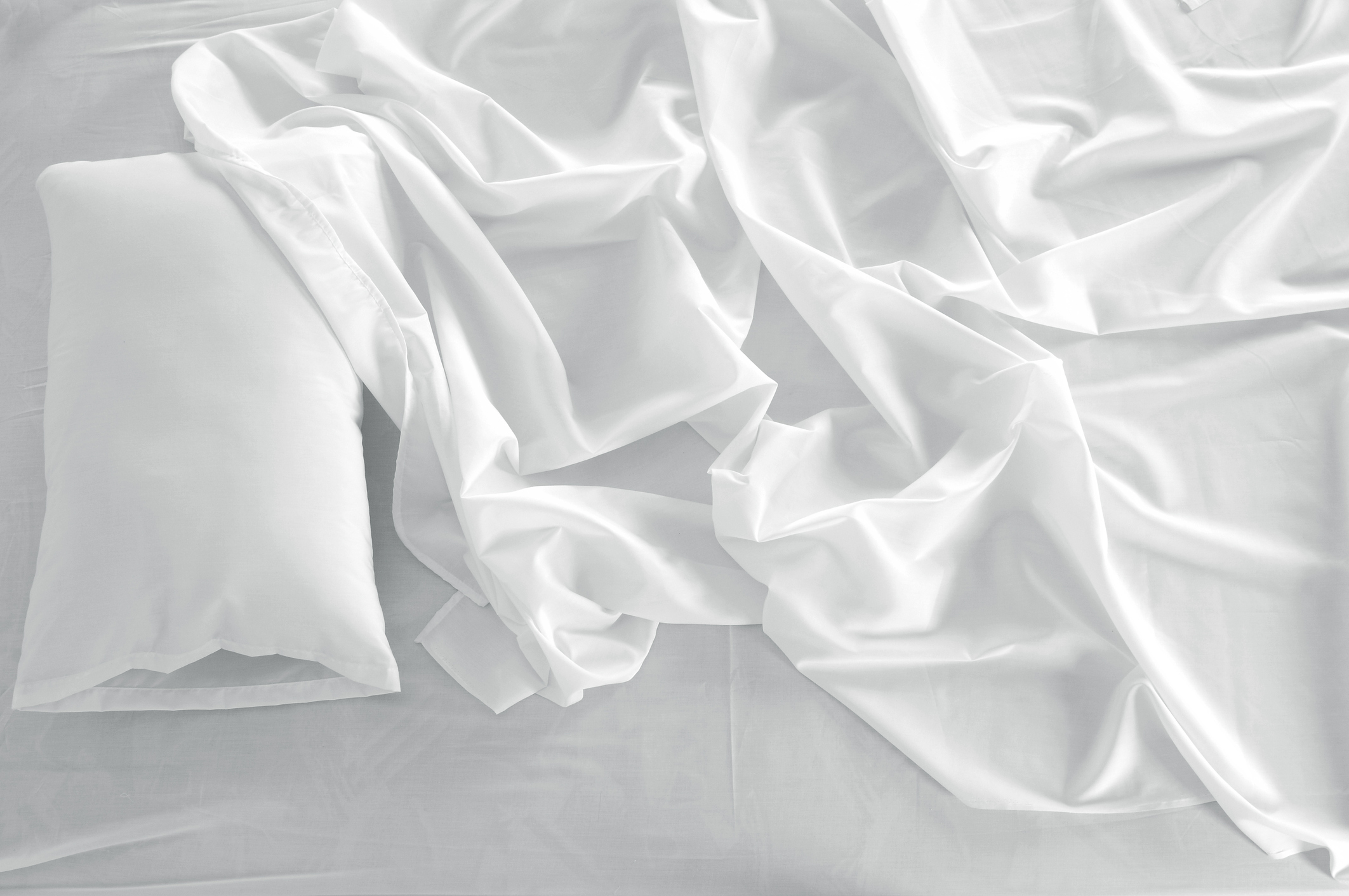 A white linen messed up bed sheets and a white pillow