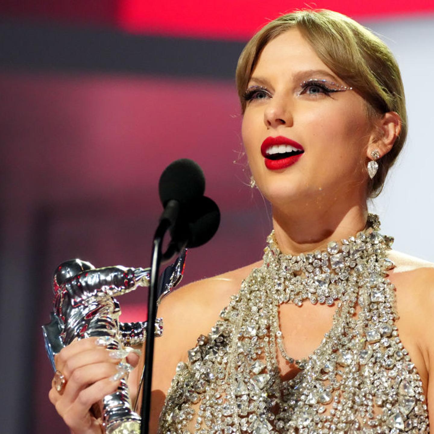 Taylor Swift, in a glittering silver dress, holds a VMAs silver statue in her right hand.