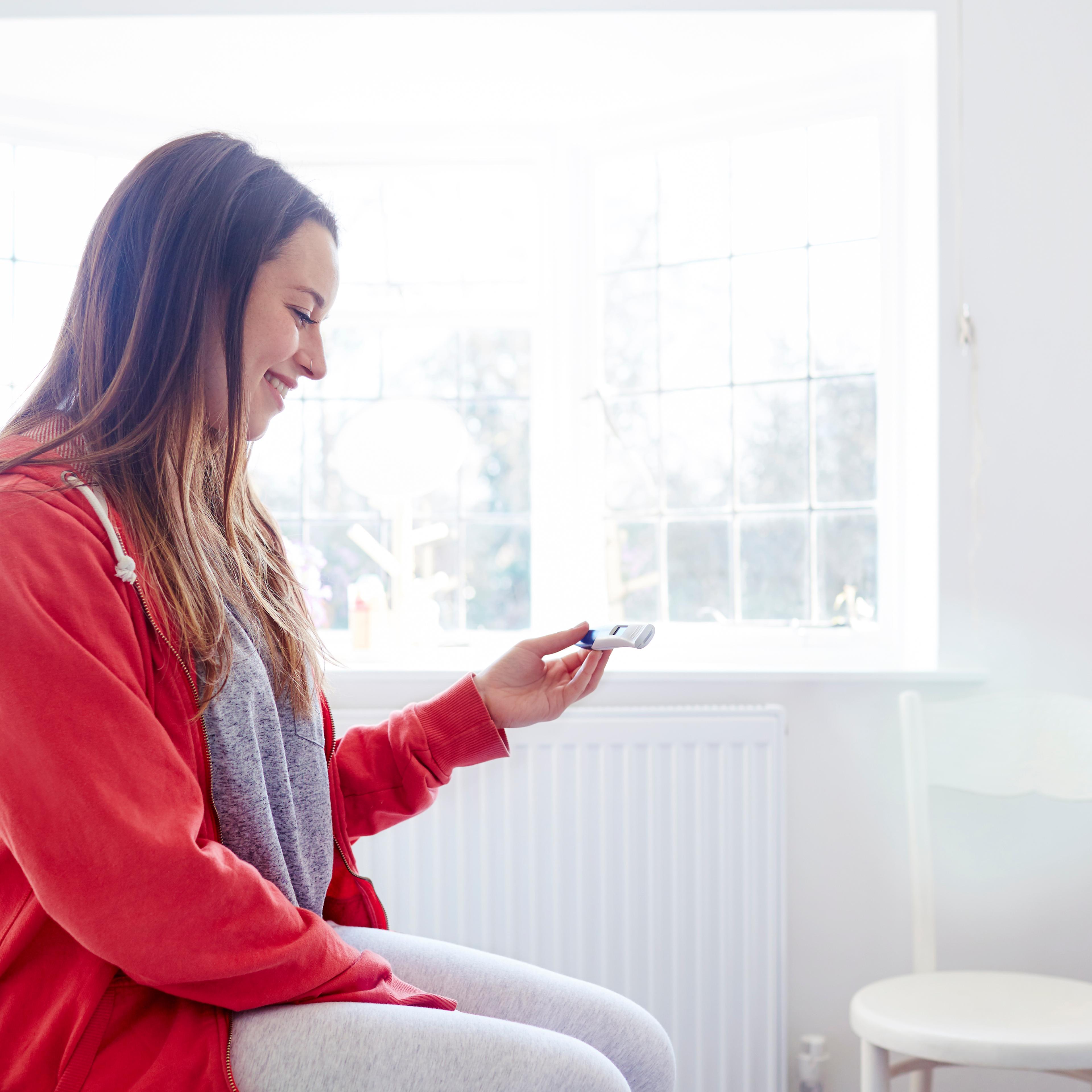 Woman sitting on bed looking at pregnancy test