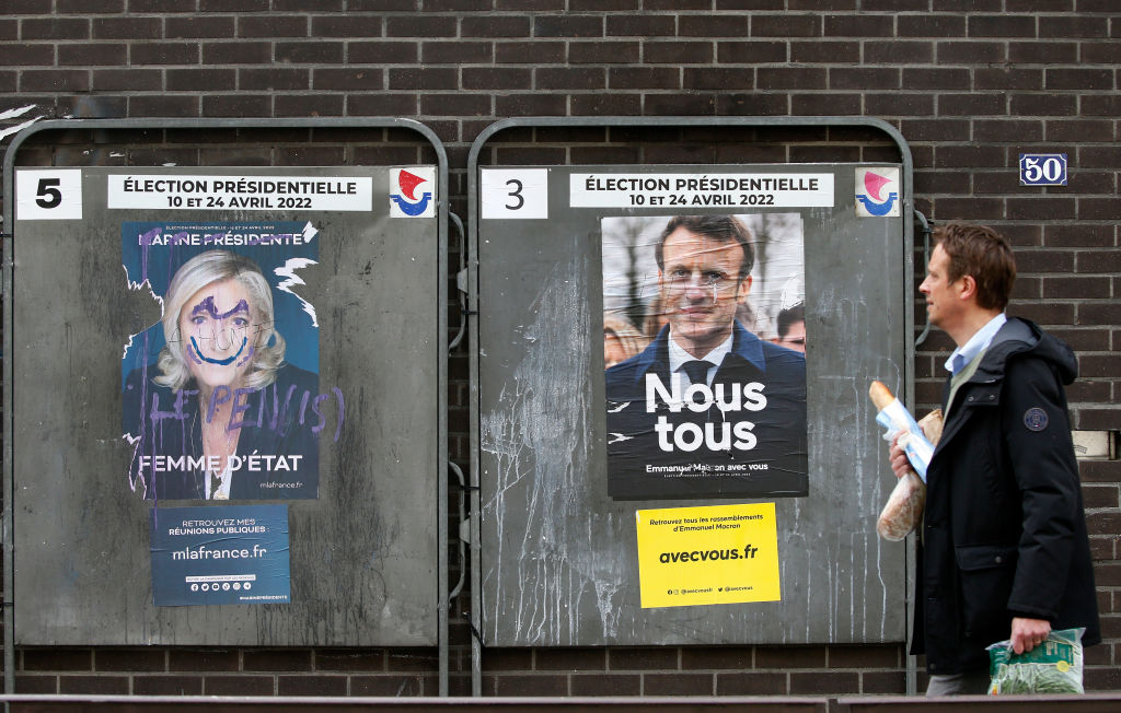 A man walks past damaged official campaign posters of Marine Le Pen, leader of the far-right Rassemblement national (RN) party and French President Emmanuel Macron 'La République en marche (LREM), candidates in the 2022 French presidential election, disp