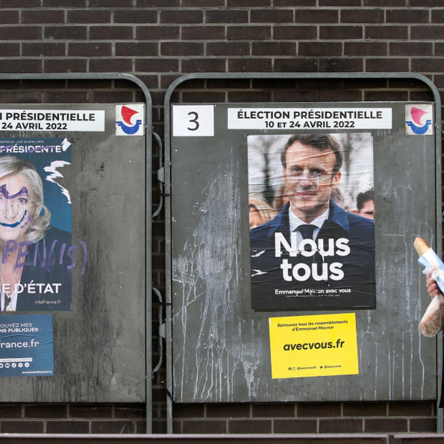 A man walks past damaged official campaign posters of Marine Le Pen, leader of the far-right Rassemblement national (RN) party and French President Emmanuel Macron 'La République en marche (LREM), candidates in the 2022 French presidential election, disp