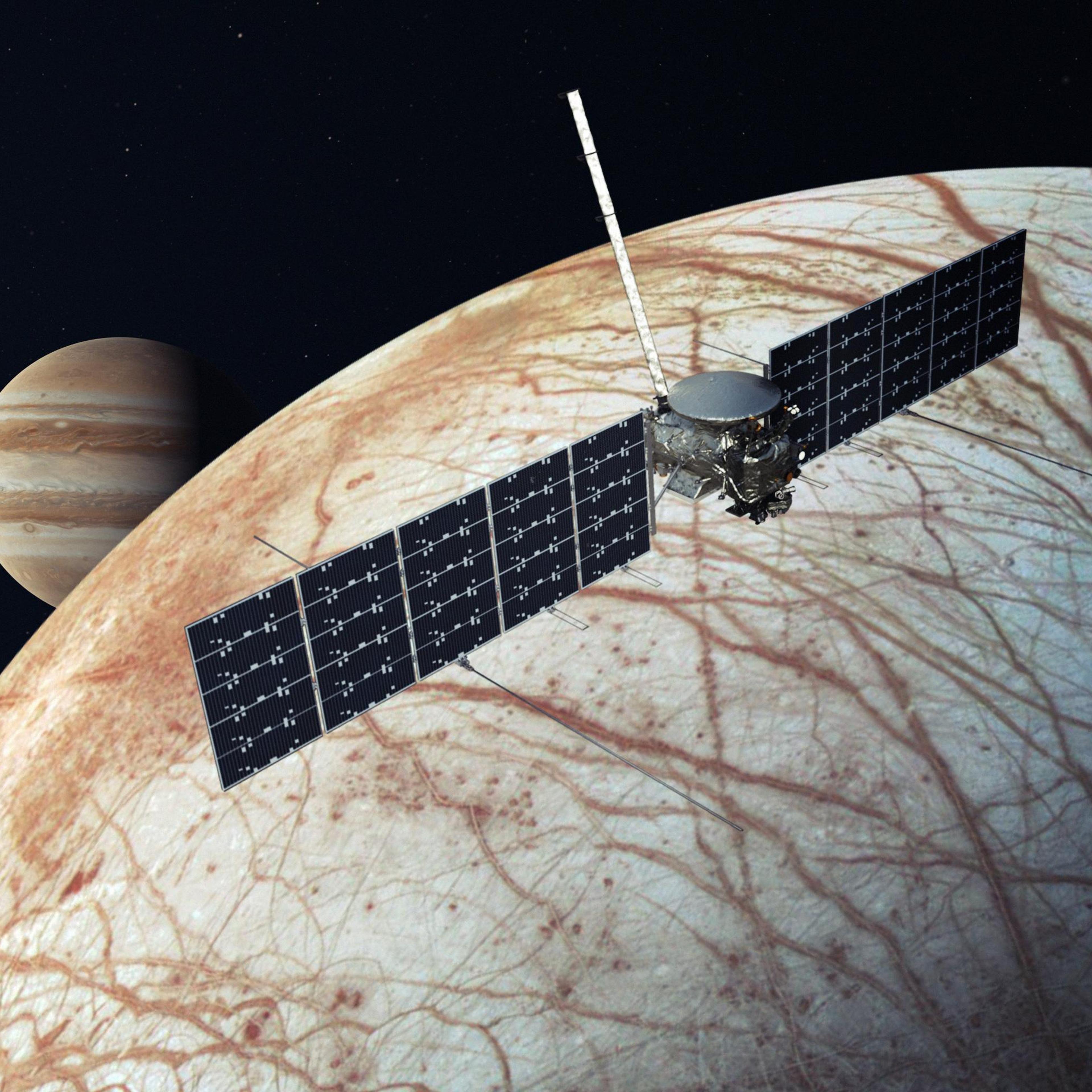 A NASA illustration depicts Europa Clipper sailing over Europa's icy, salt-stained surface with Jupiter in the background