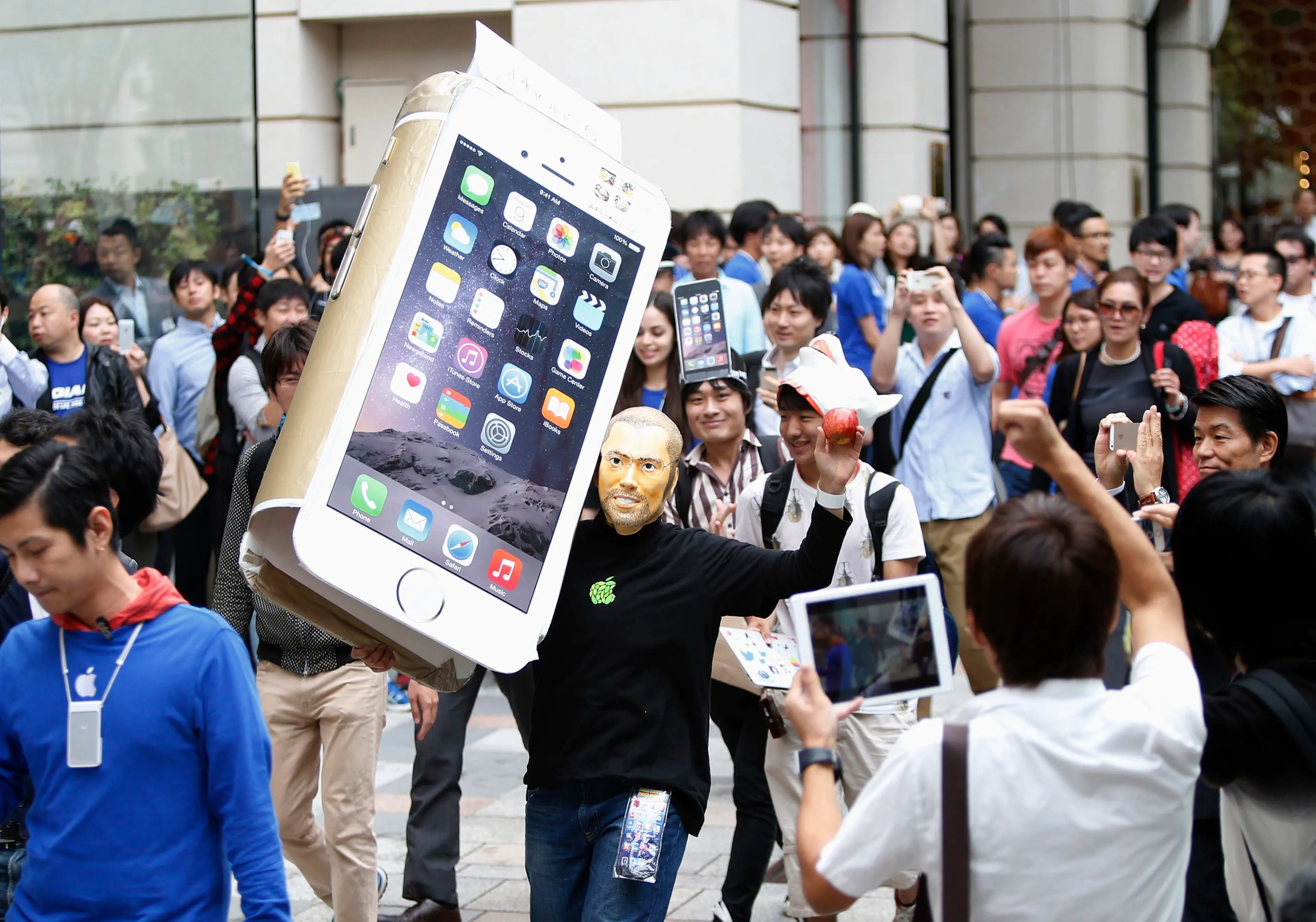 A man wearingaA man wearing a mask depicting Apple's co-founder Steve Jobs holds up a cardboard cut-out of Apple's new iPhone 6, as he walks into the Apple Store in Tokyo on Sept. 18, 2014. a mask depicting Steve Jobs holds up a cardboard cut-out of Appl