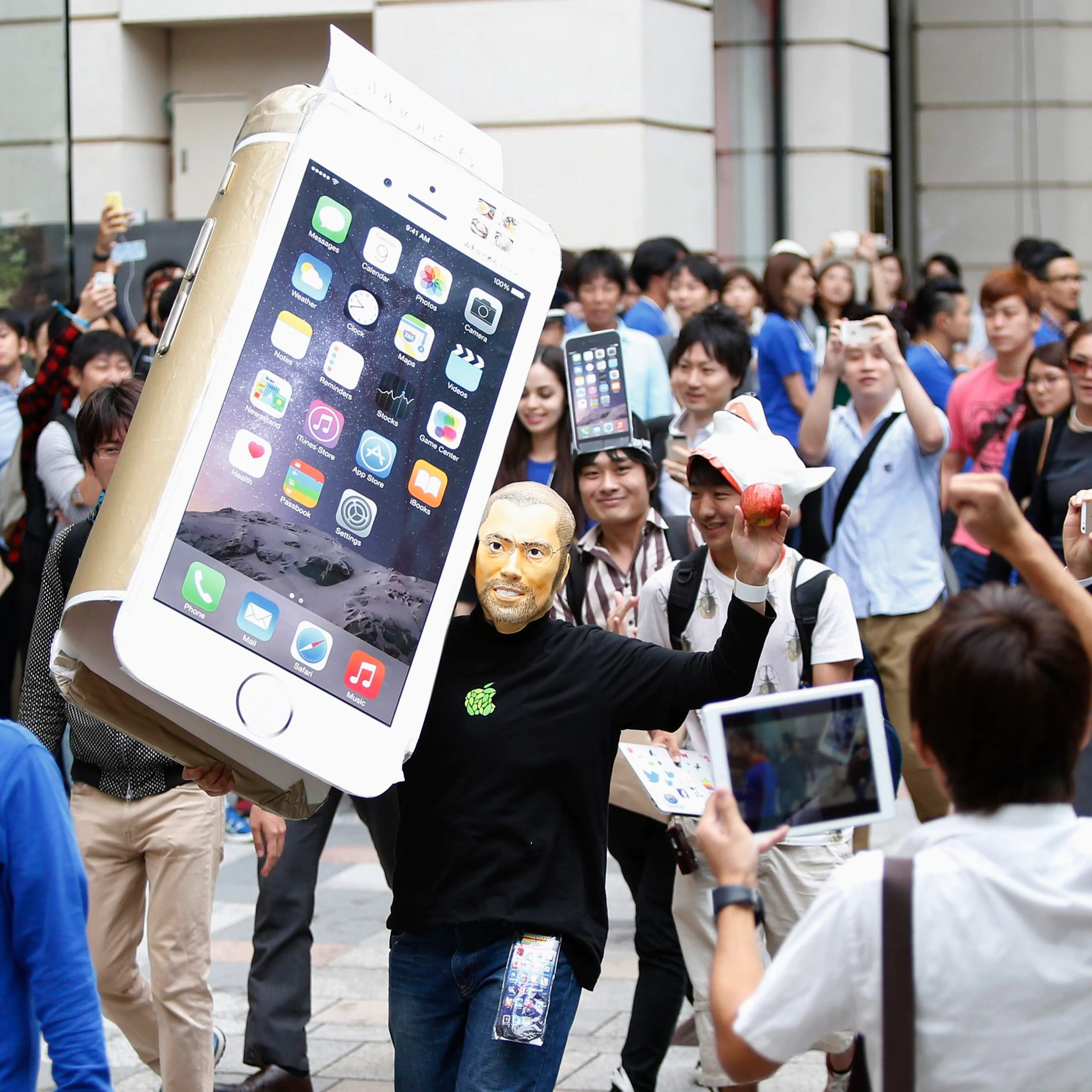 A man wearingaA man wearing a mask depicting Apple's co-founder Steve Jobs holds up a cardboard cut-out of Apple's new iPhone 6, as he walks into the Apple Store in Tokyo on Sept. 18, 2014. a mask depicting Steve Jobs holds up a cardboard cut-out of Appl