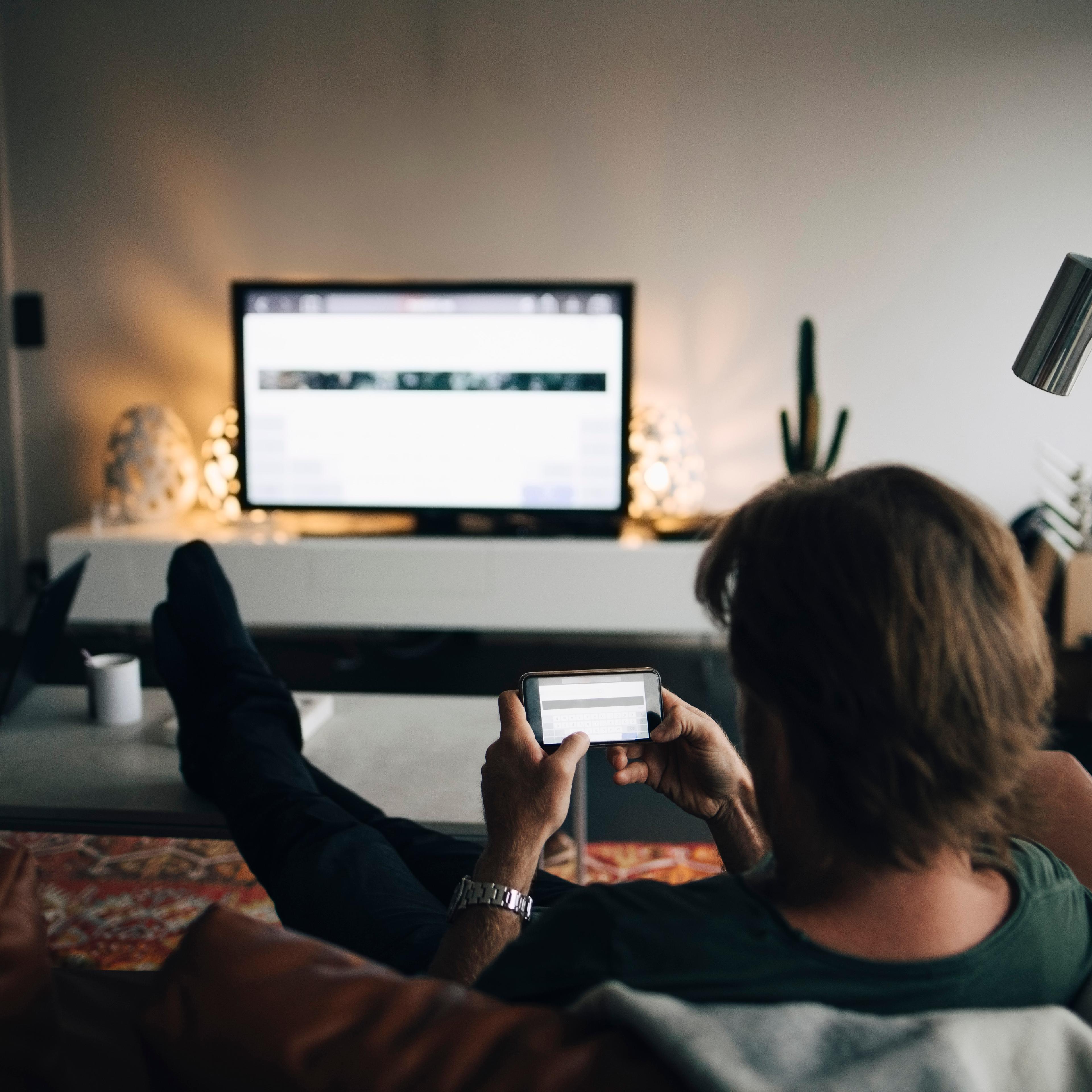 Full length of man using mobile phone while sitting on sofa in living room