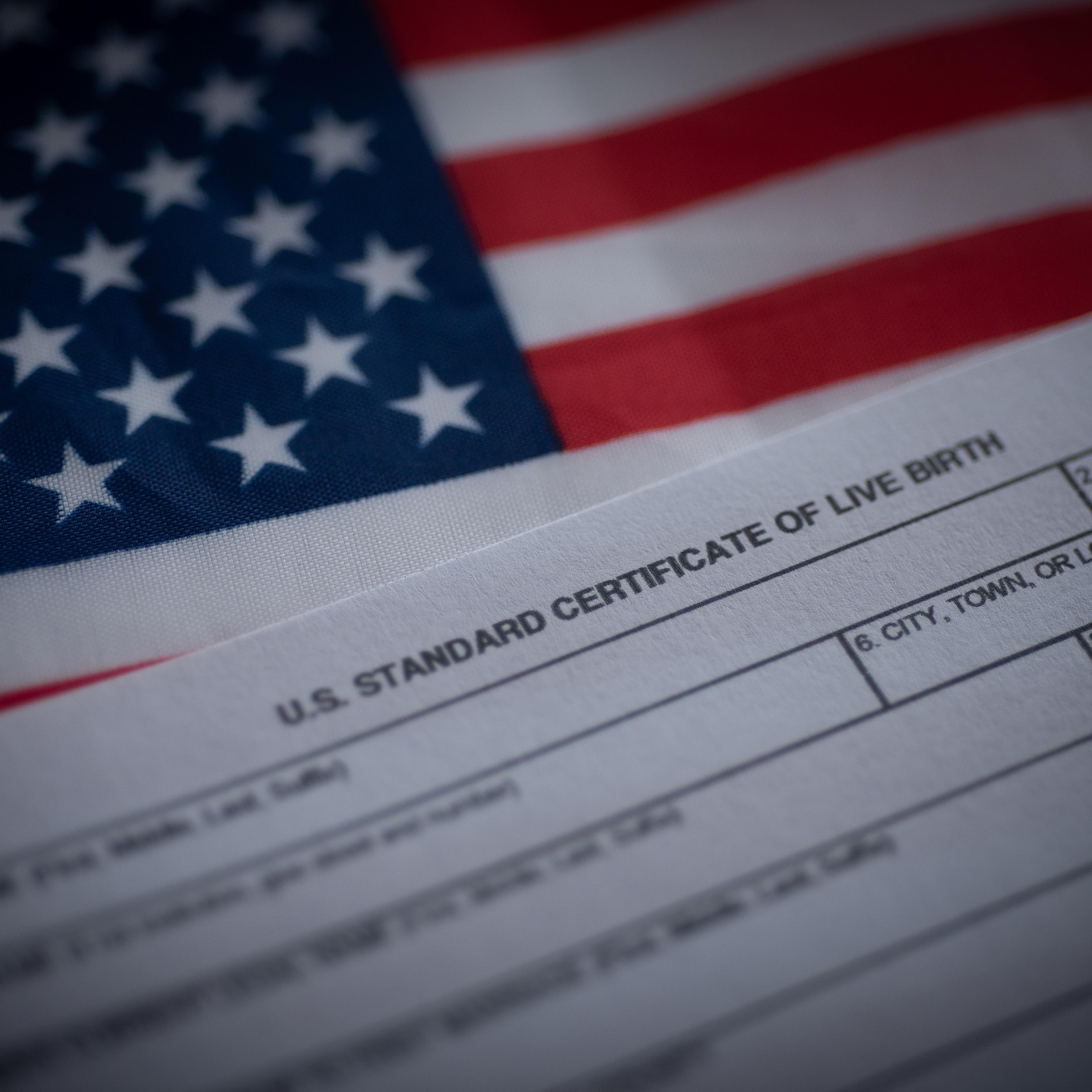 U.S. standard certificate of live birth application form next to flag of USA. Birthright citizenship concept.
