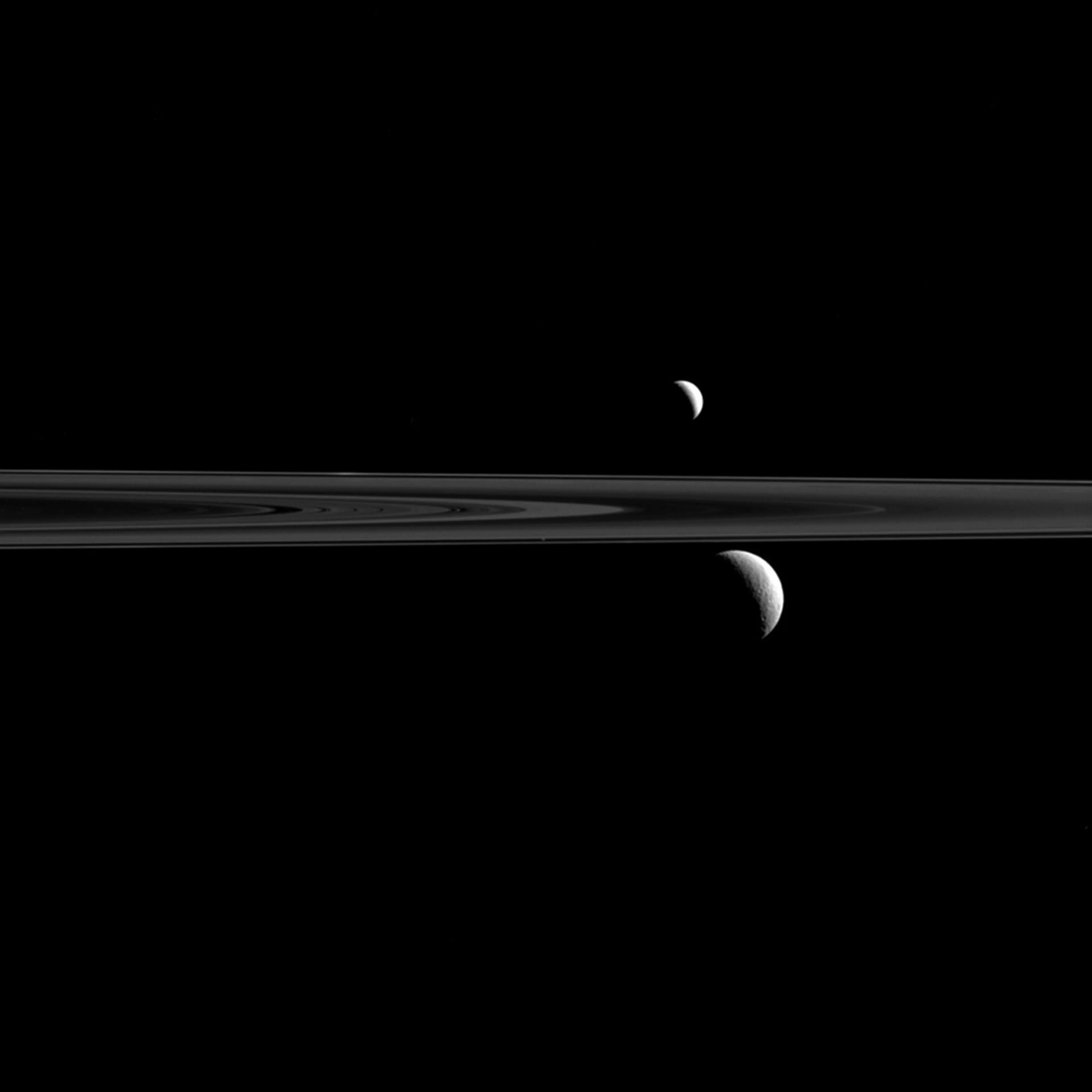 The Cassini spacecraft captures Enceladus above Saturn's rings and Rhea below. The tiny speck of Atlas can also be seen just above and to the left of Rhea, and just above the thin line of Saturn's F ring. The image was taken in visible light with the Cas