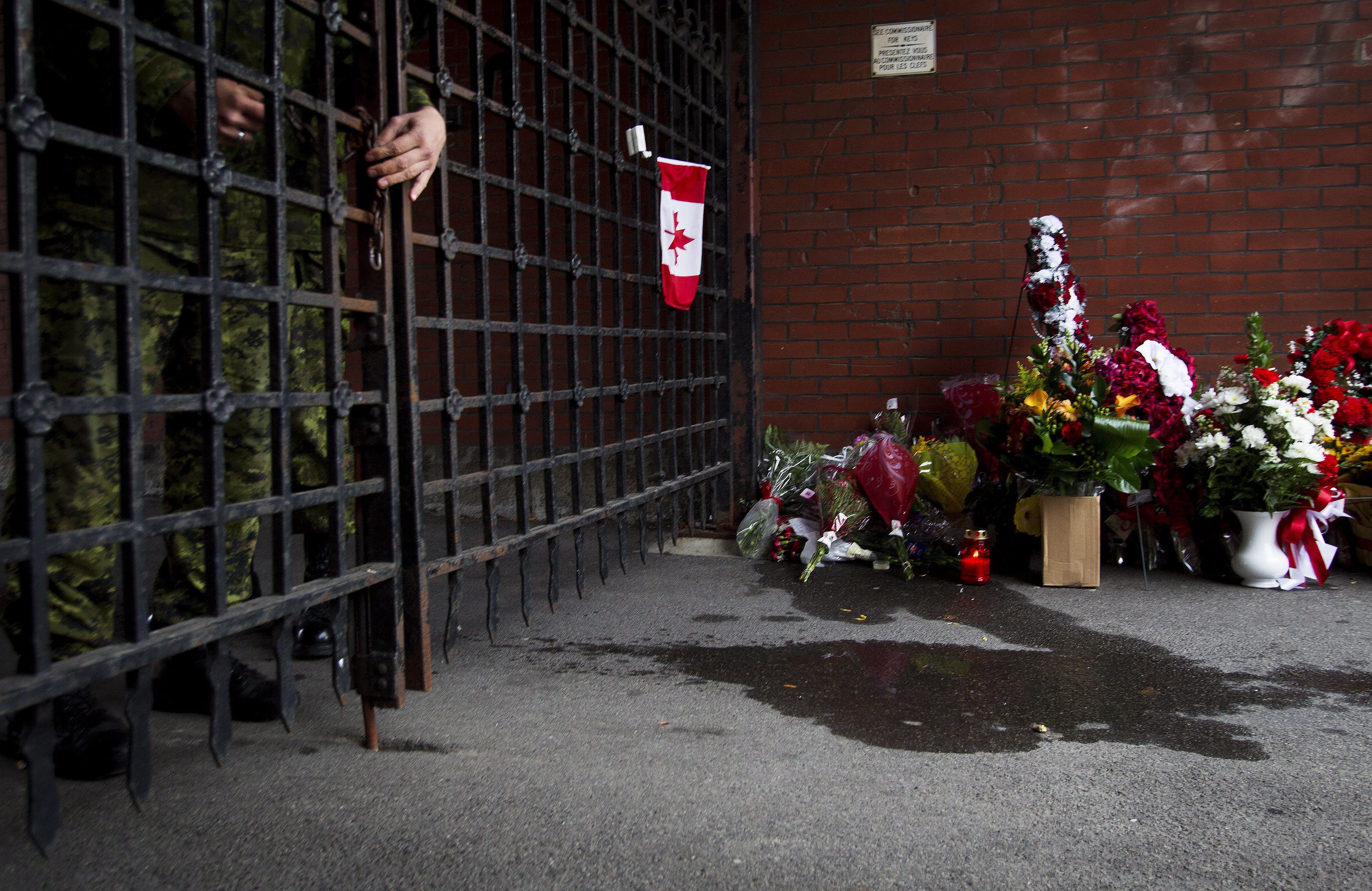A soldier locks the gates as flowers are placed at a memorial outside the gates of the John Weir Foote Armory, the home of the Argyll and Sutherland Highlanders of Canada in Hamilton, Ontario on Oct. 22, 2014, in memory of Canadian soldier Nathan Cirillo