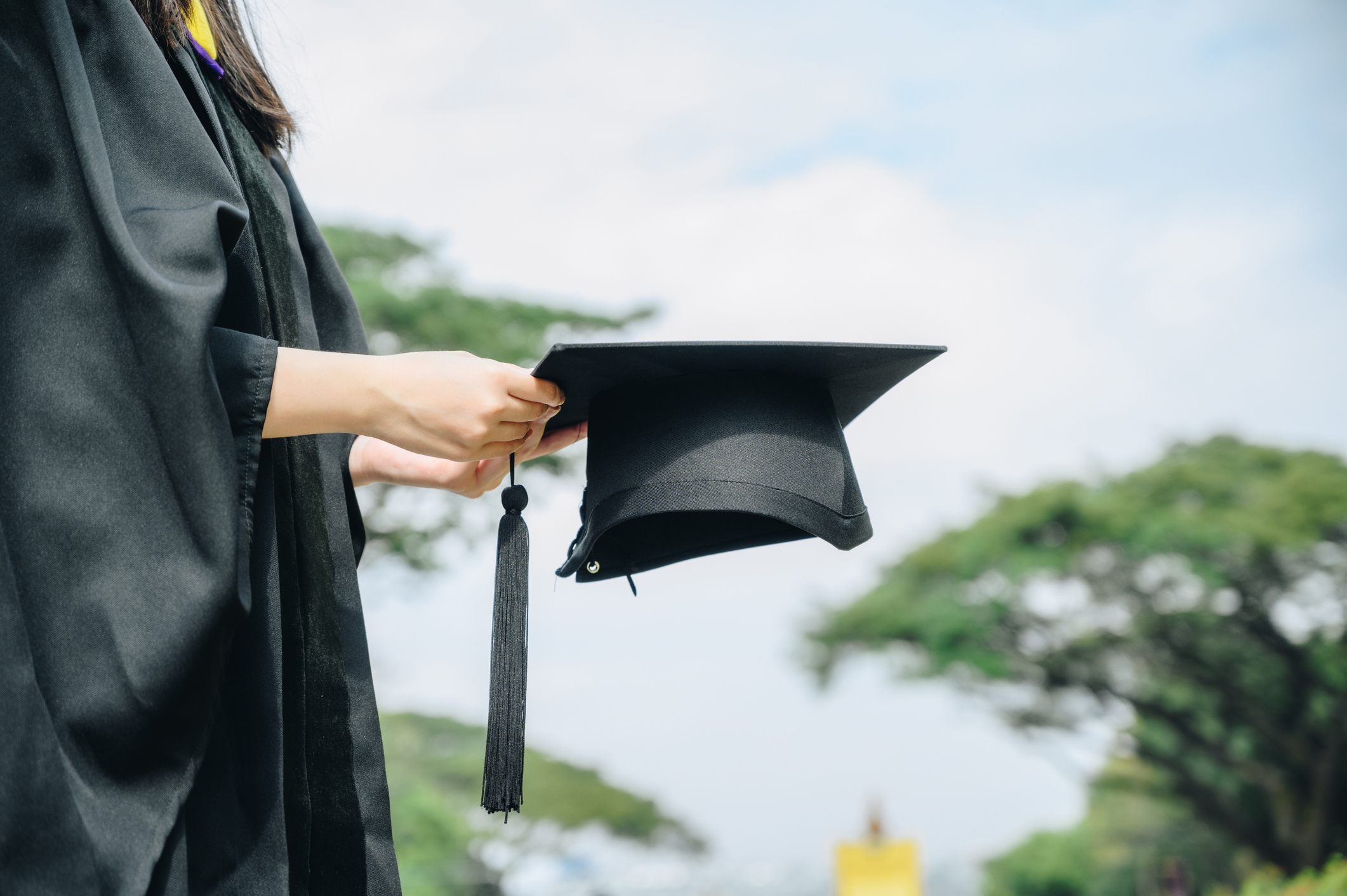 Student wearing graduation gown and holding a graduation cap.