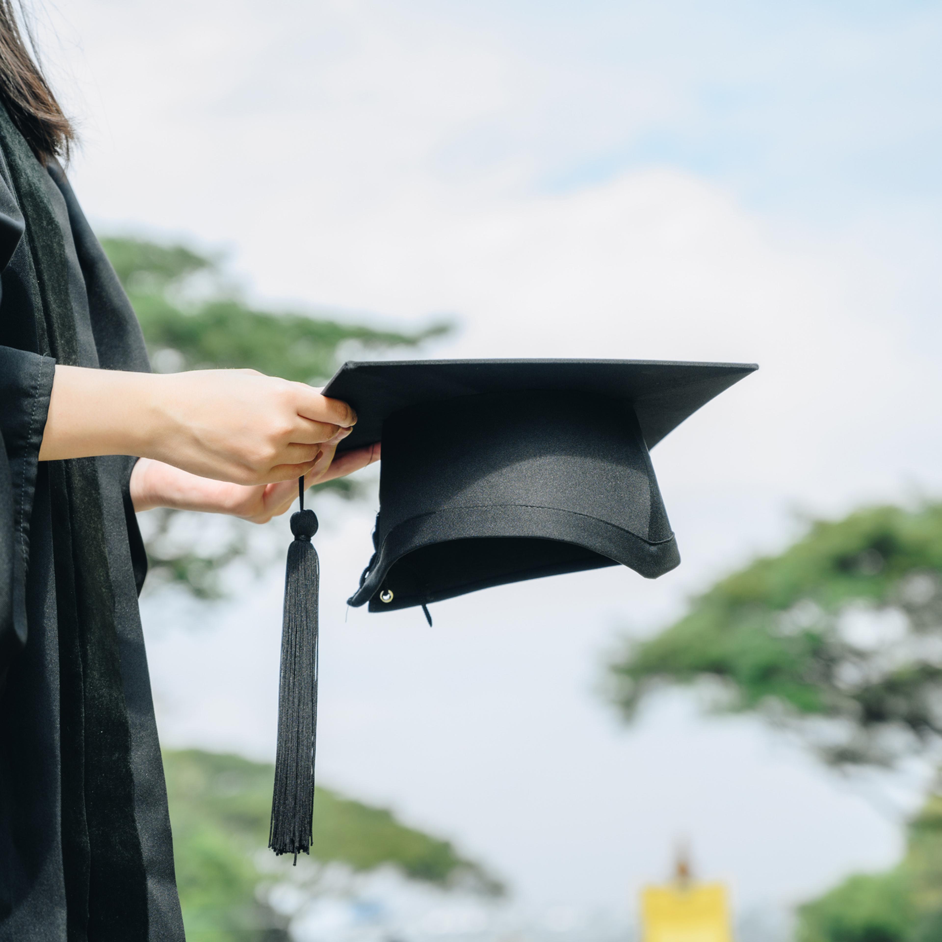 Student wearing graduation gown and holding a graduation cap.