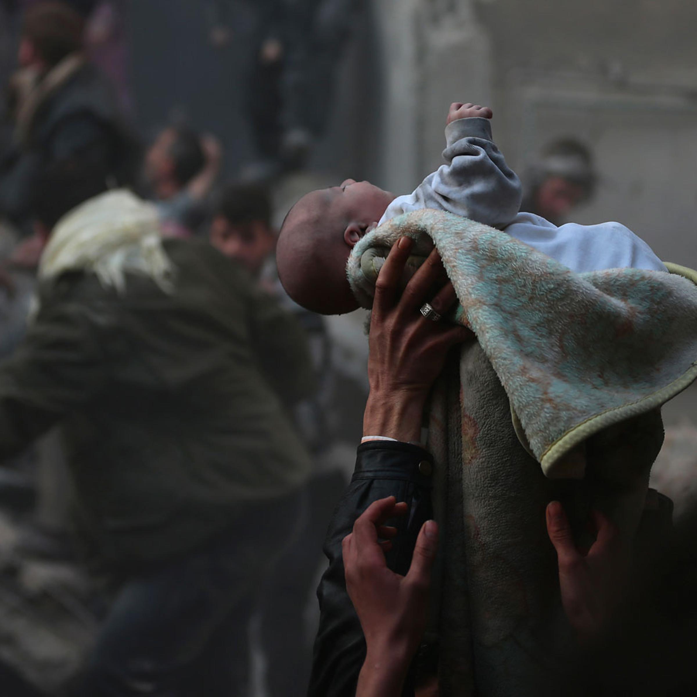 Men hold up a baby saved from under rubble, who survived an airstrike in the Duma neighbourhood of Damascus