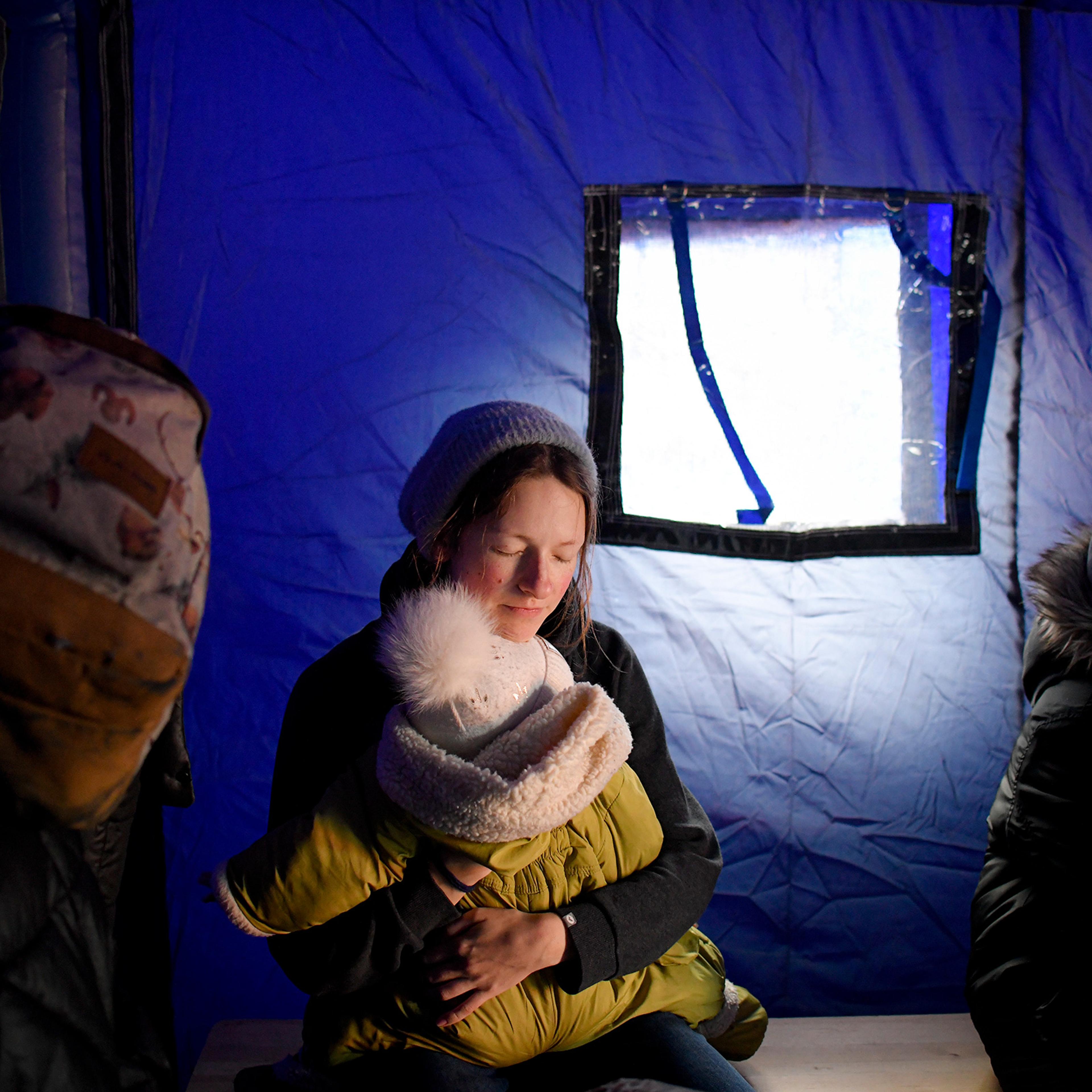 A refugee fleeing Ukraine holds her baby as she sits in a tent at the border in Siret, Romania on Feb. 26