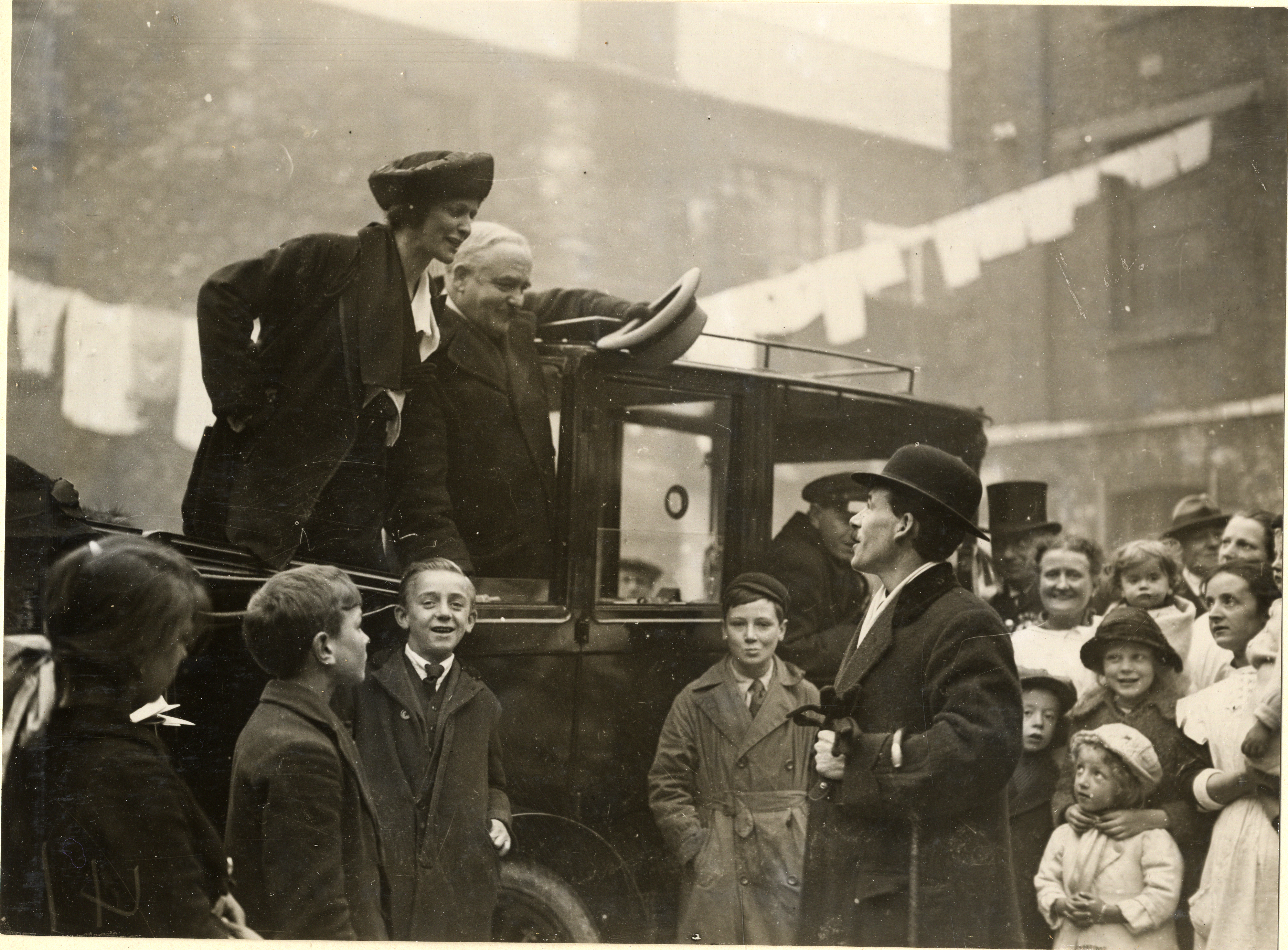 A photograph of Nancy Astor standing in the back of a car and talking to a man in the crowd at Clare Buildings, Coxside 