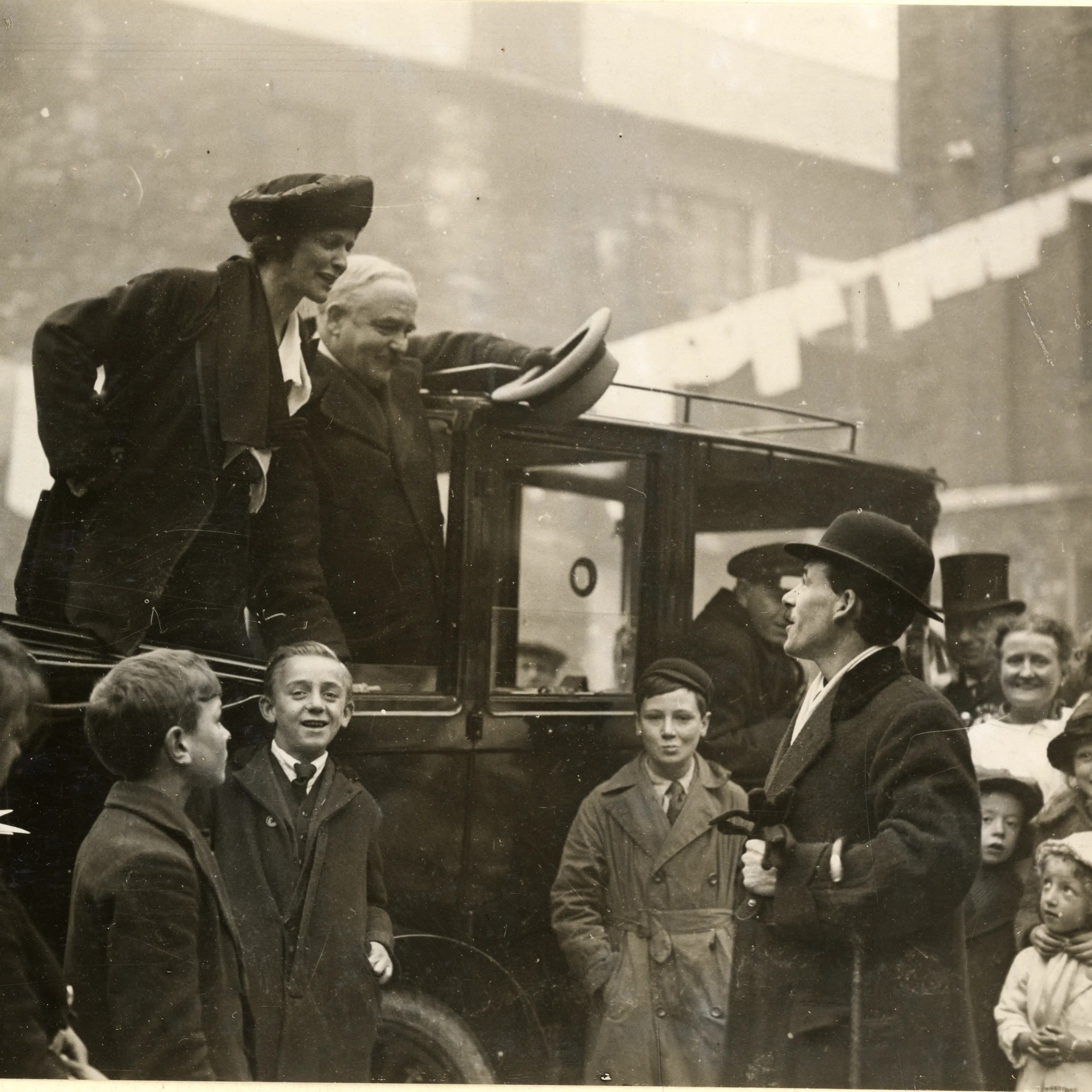 A photograph of Nancy Astor standing in the back of a car and talking to a man in the crowd at Clare Buildings, Coxside