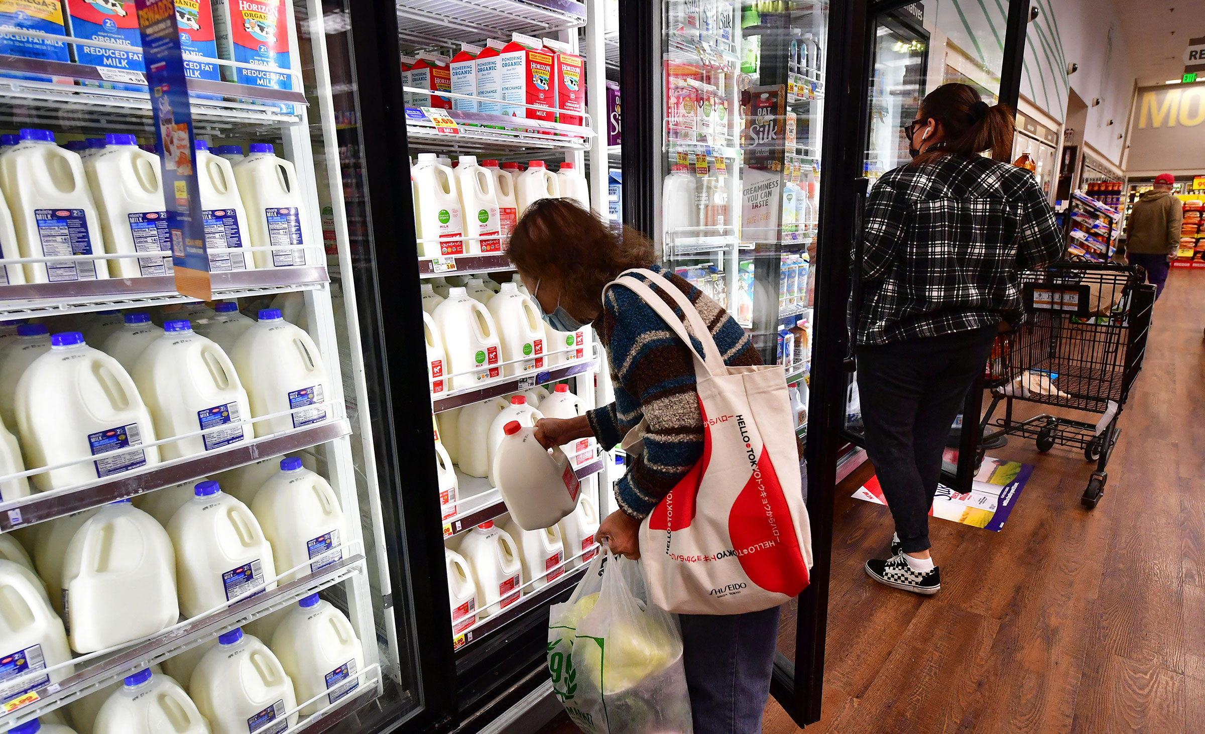 A person pulls out a gallon of milk as people shop at a grocery store in Monterey Park, Calif, on April 12, 2022.