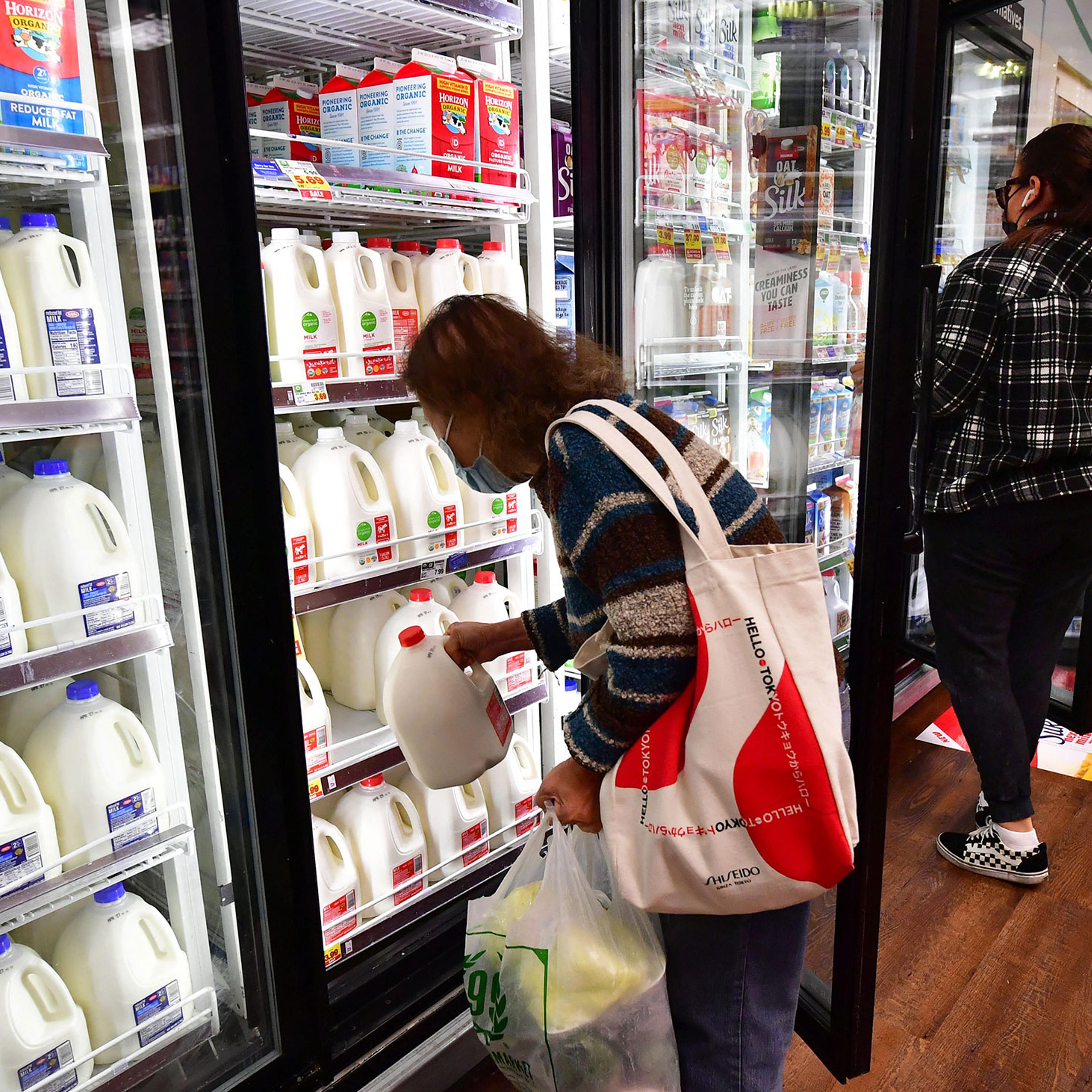 A person pulls out a gallon of milk as people shop at a grocery store in Monterey Park, Calif, on April 12, 2022.