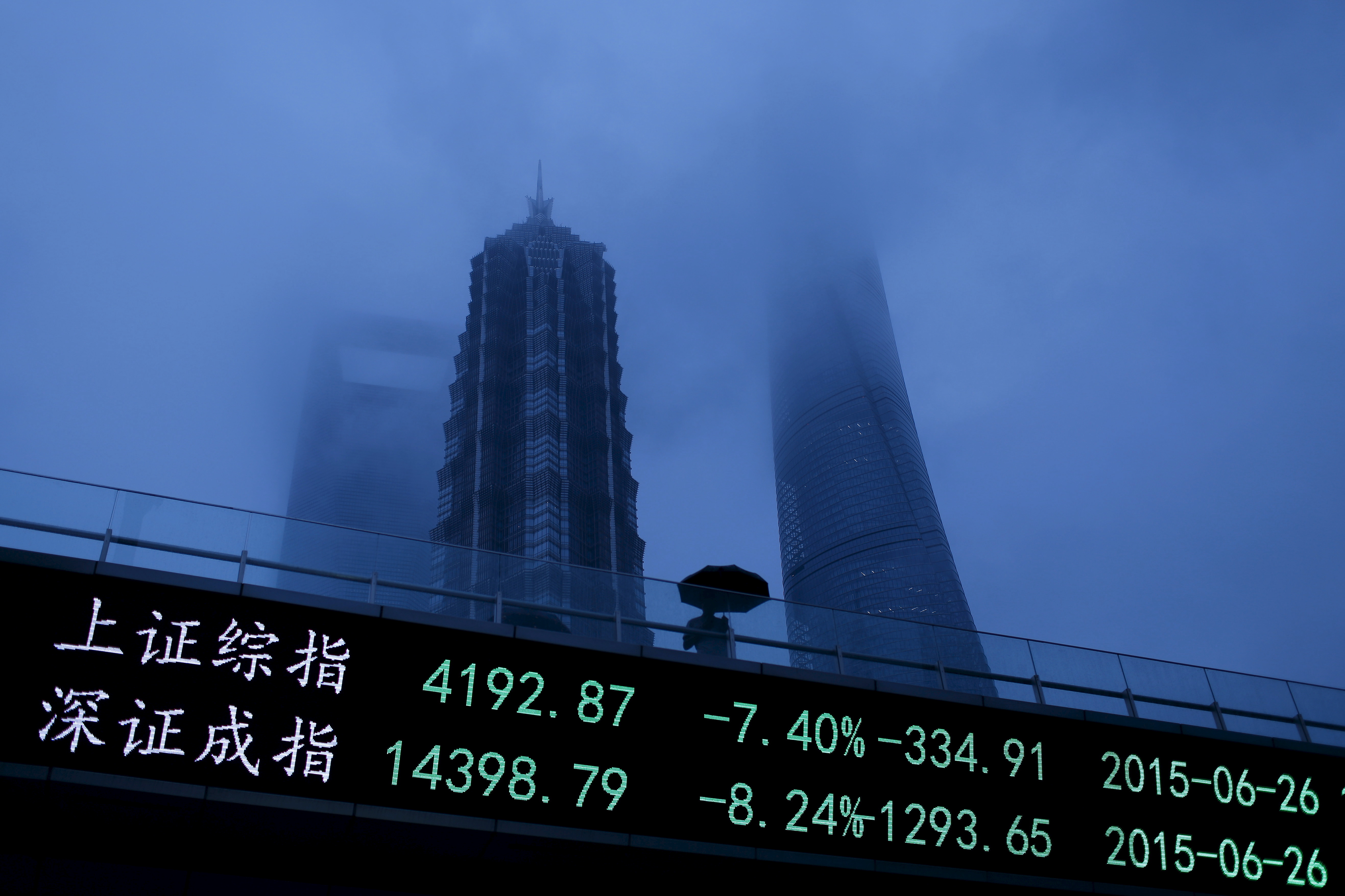 A man walks past an electronic board showing the benchmark Shanghai and Shenzhen stock indices, on a pedestrian overpass at the Pudong financial district in Shanghai