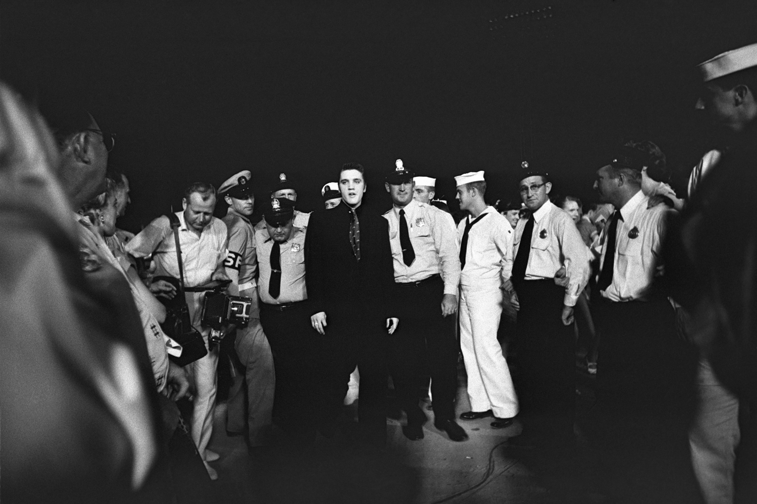 July 4, 1956. Russwood Park, Memphis. Elvis is entering the stadium escorted by the local police and fire department, but also by the Shore Police of the Navy. This was Elvis' first charitable benefit show, with proceeds going to The Cynthia Milk Fund and the Variety Club’s Home for Convalescent Children.