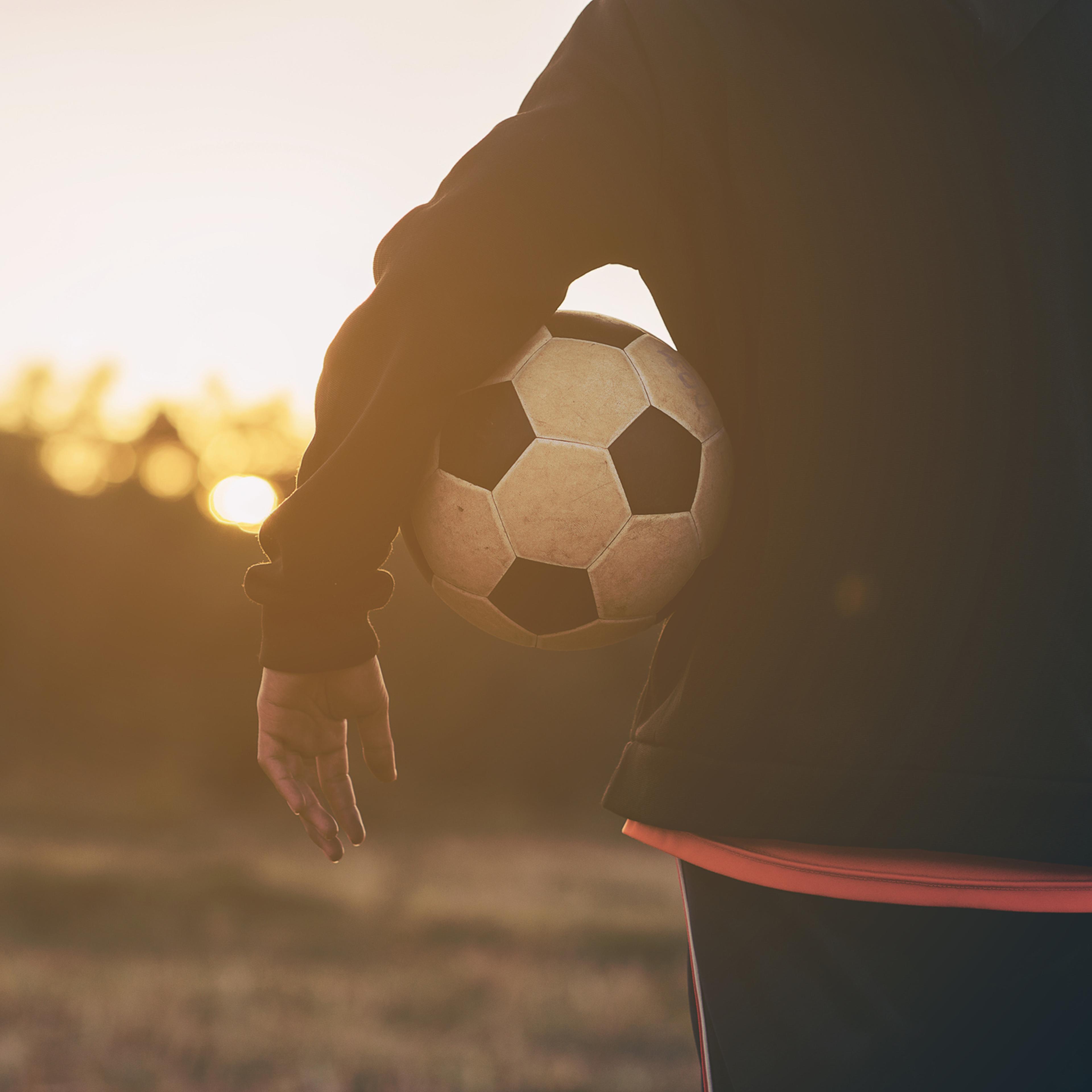 Midsection Of Woman Holding Soccer Ball While Standing On Field During Sunset