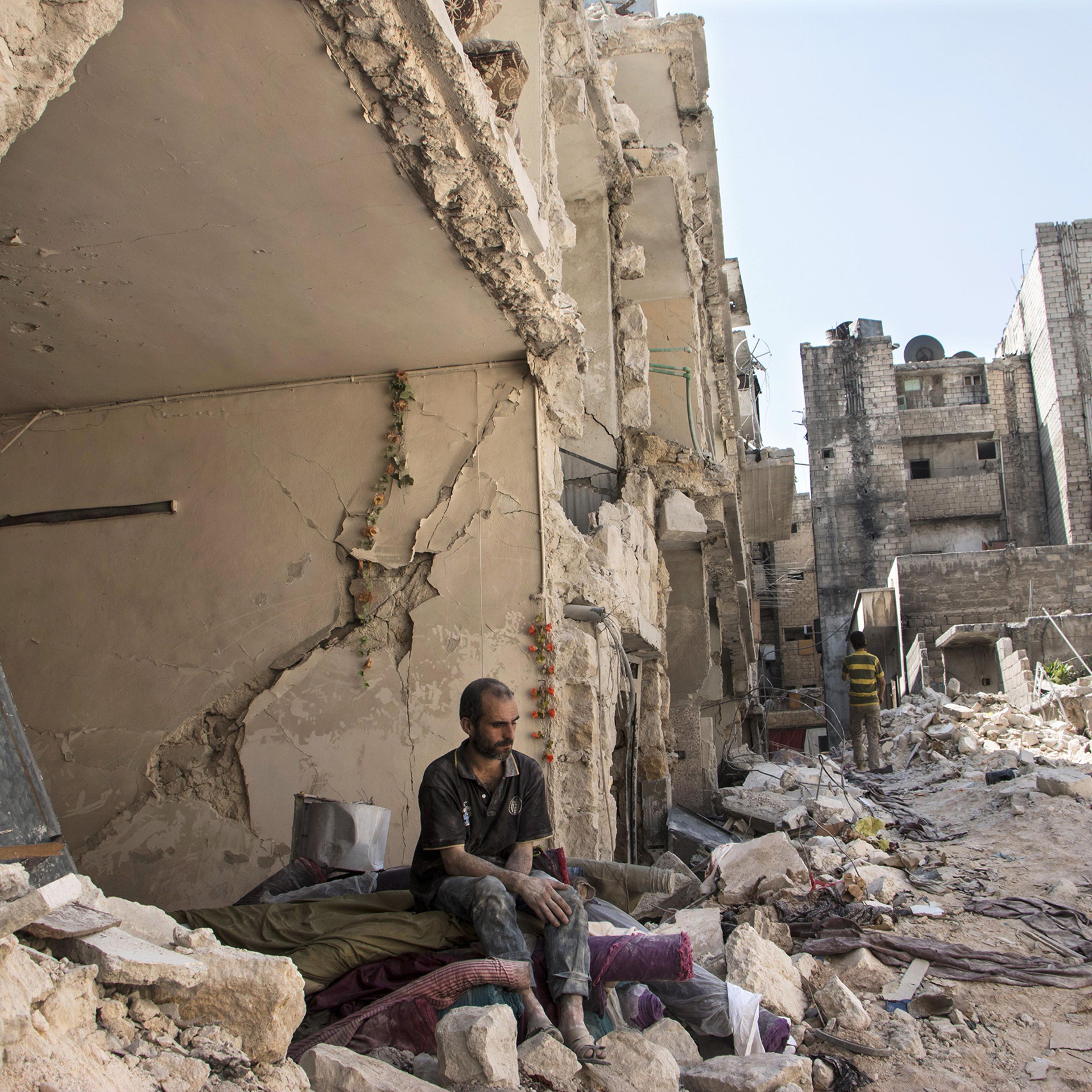 A Syrian man sits in the rubble following a barrel bomb attack the previous day on the rebel-held neighborhood of al-Mashad in Aleppo on Sept. 17, 2015.