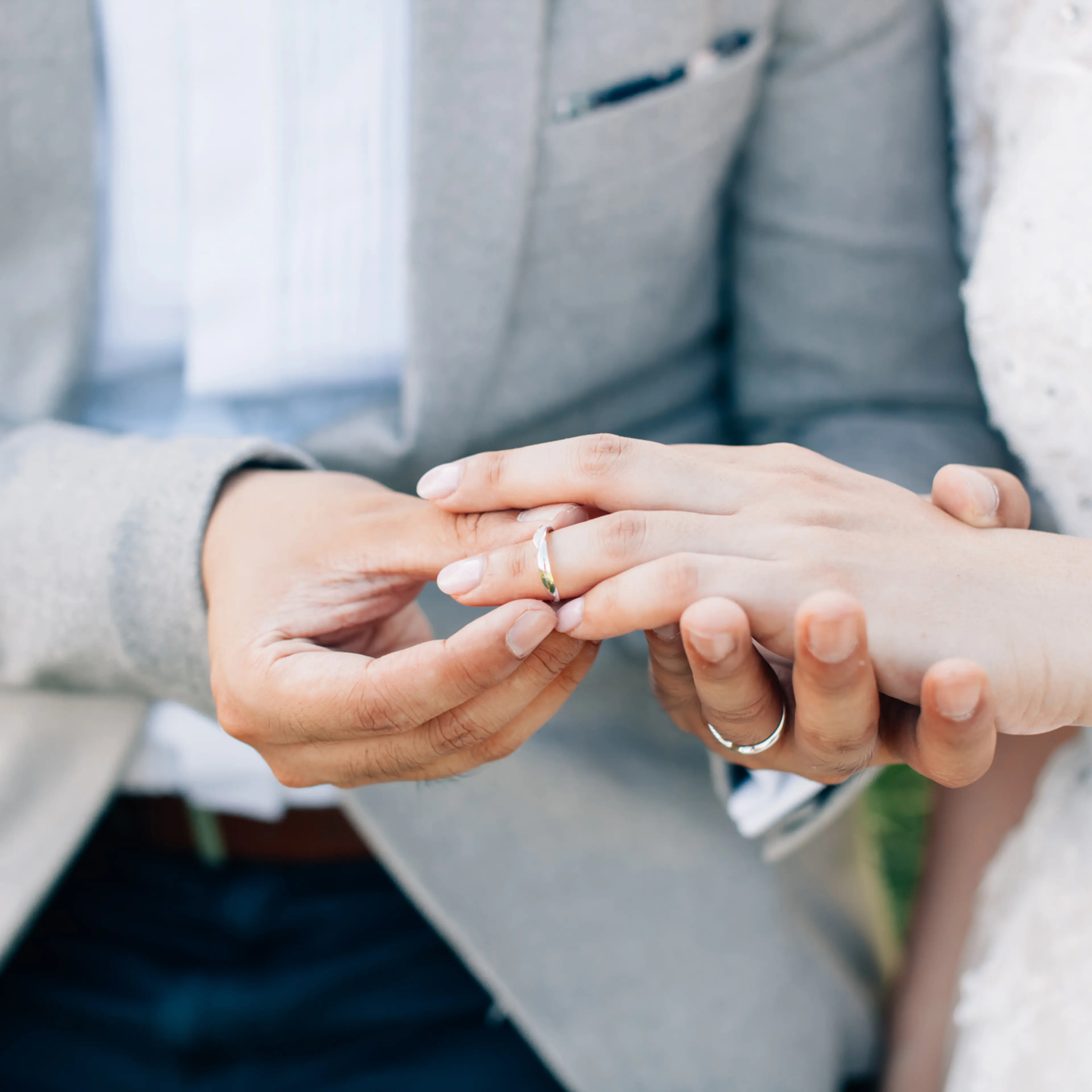 Groom putting ring on bride's finger. Rings exchange. Happy couple celebrating wedding outdoors.