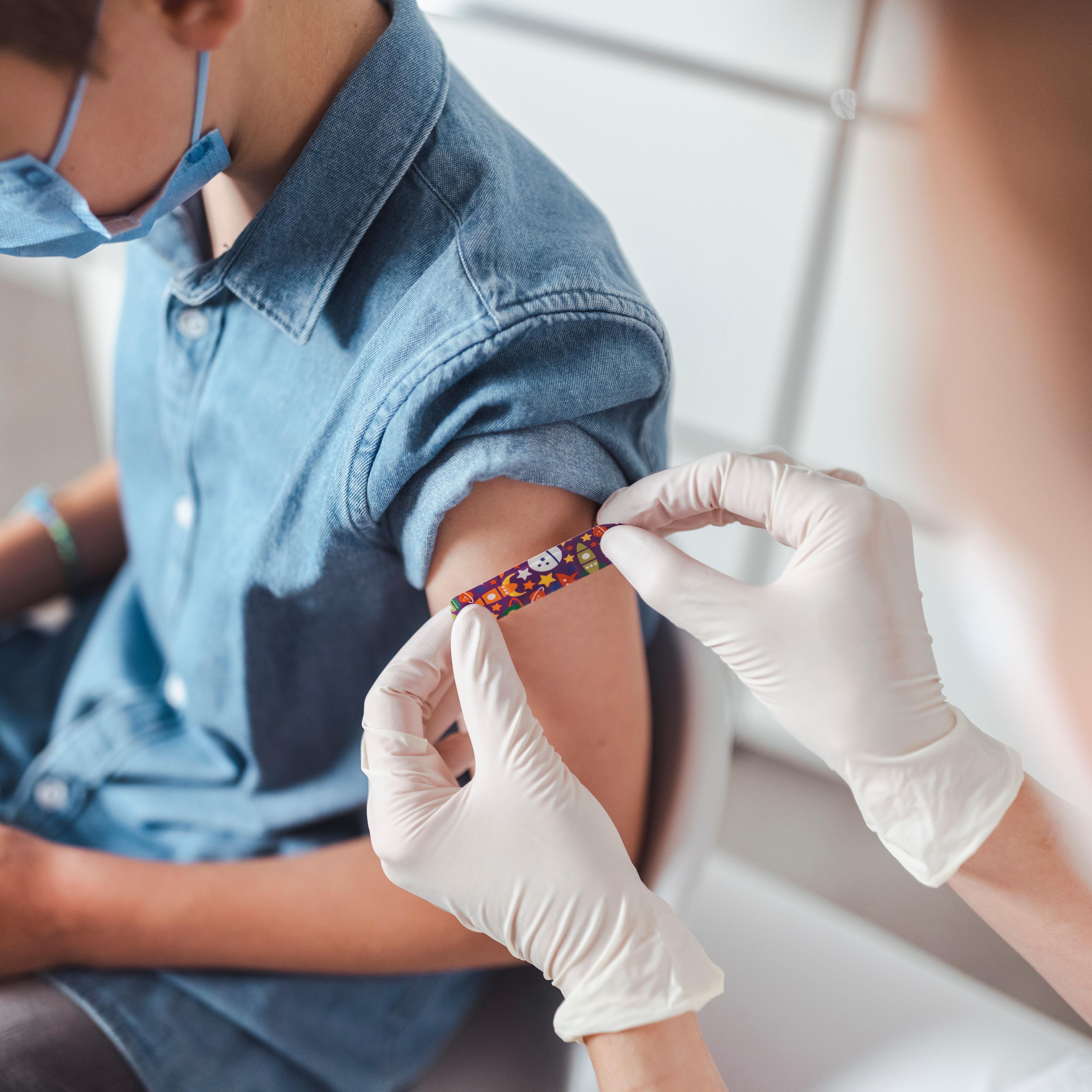 Nurse putting adhesive bandage on boy's arm at vaccination center
