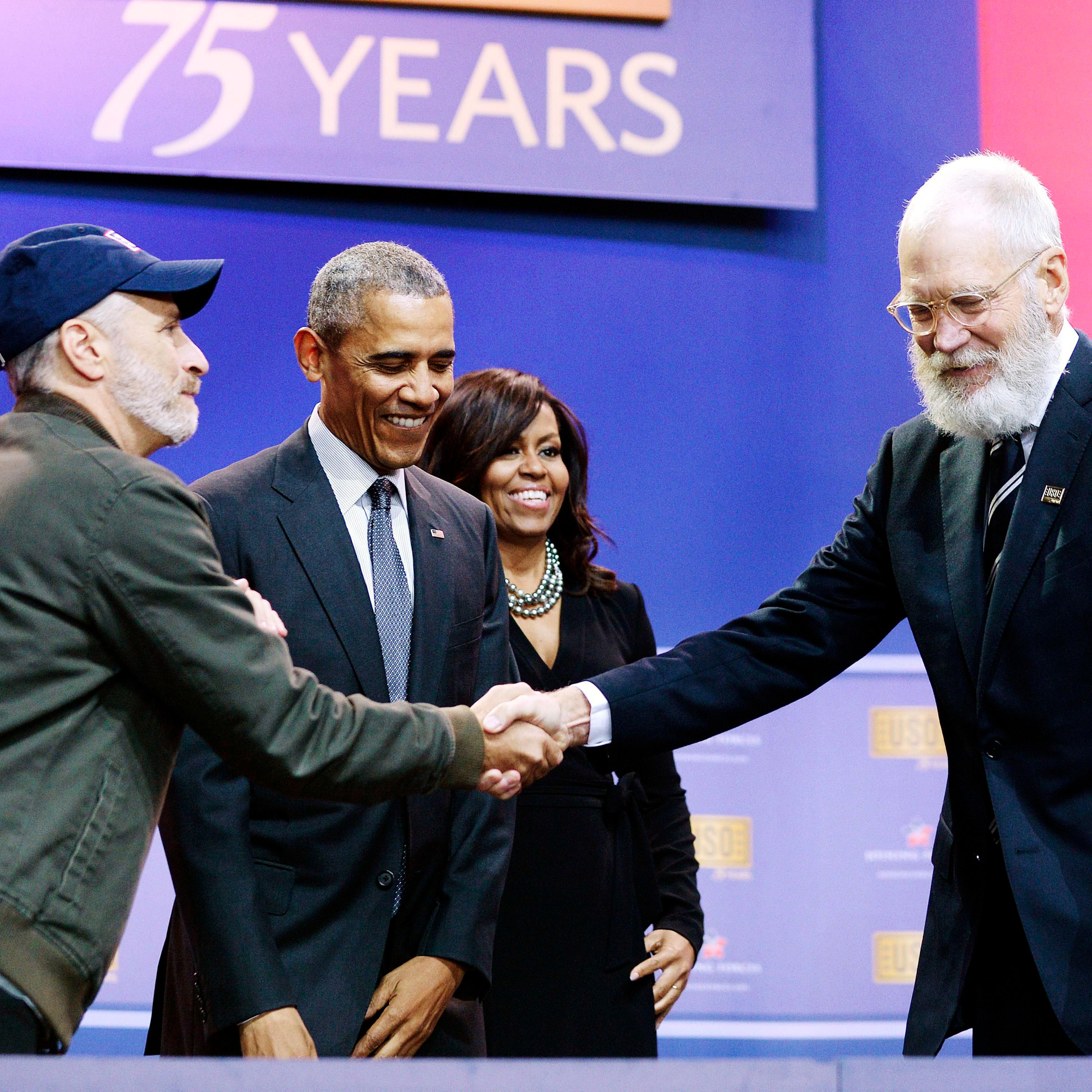 Comedian Jon Stewart shakes hands with comedian David Letterman as President Barack Obama and First Lady Michelle Obama watch at the 75th anniversary of the USO at Joint Base Andrews in Maryland on May 5, 2016.
