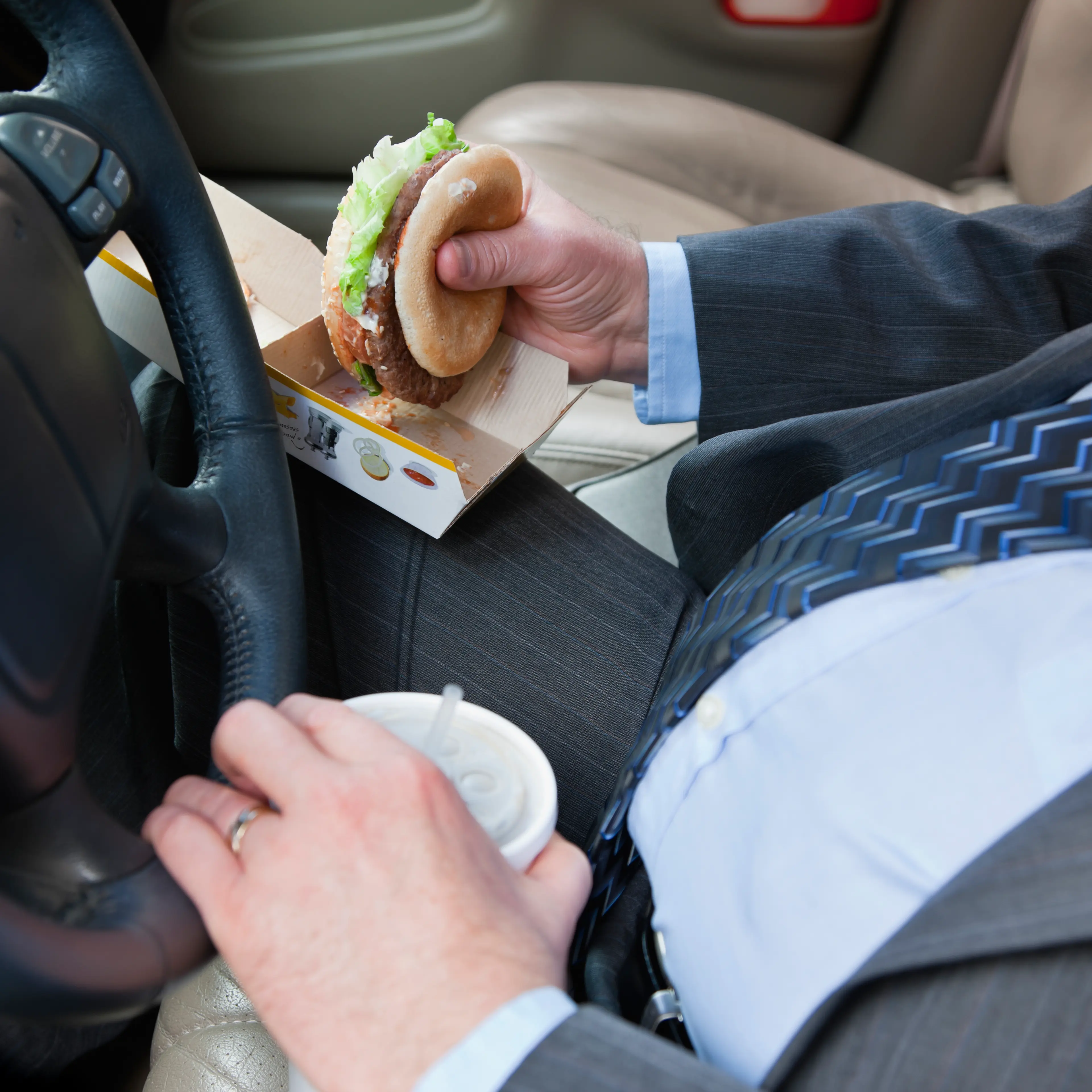 man driving a car, eating a burger