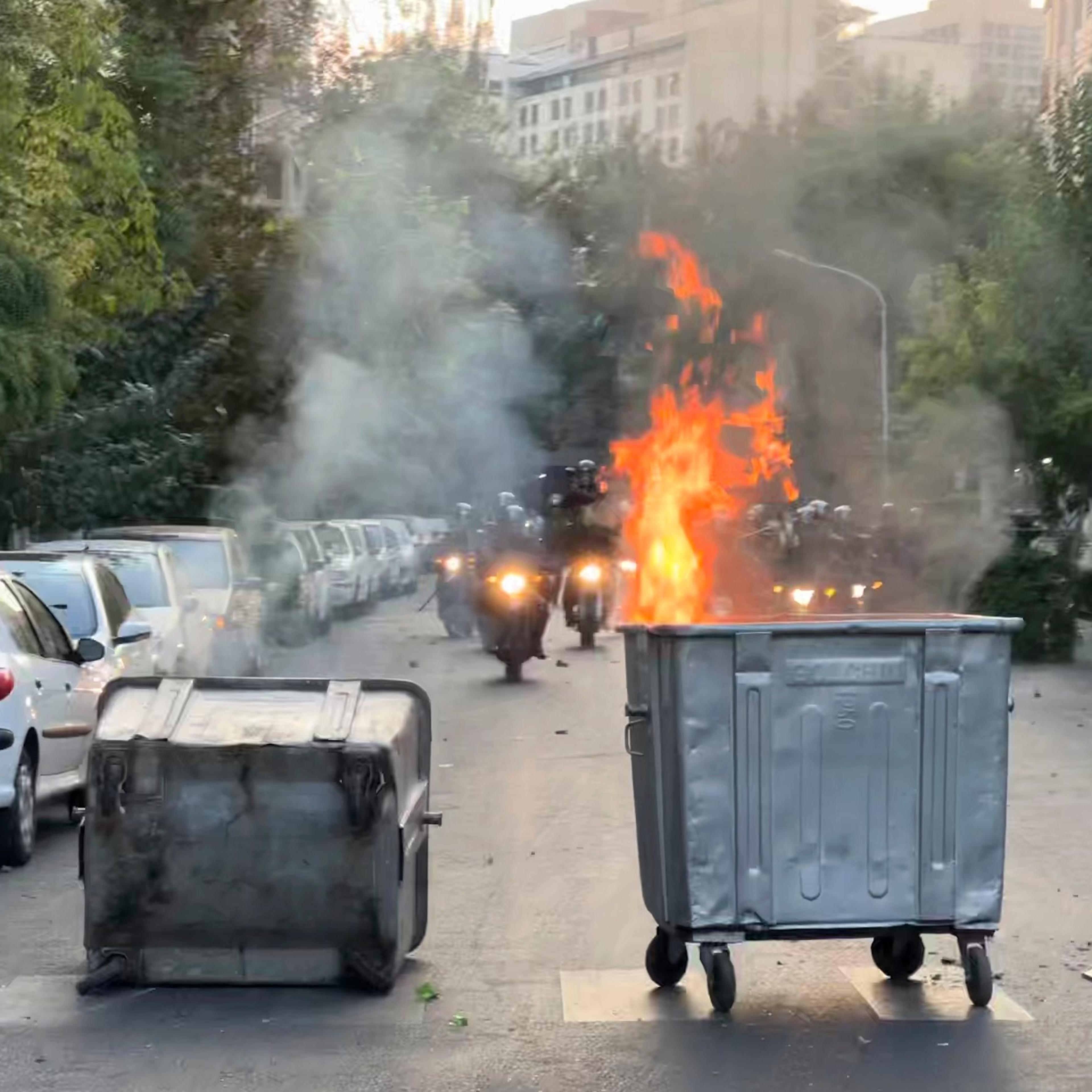 A trash bin is burning as anti-riot police arrive on Sept. 20 during a protest over the death of a young woman, Mahsa Amini, who had been detained for violating the country's conservative dress code, in downtown Tehran, Iran.