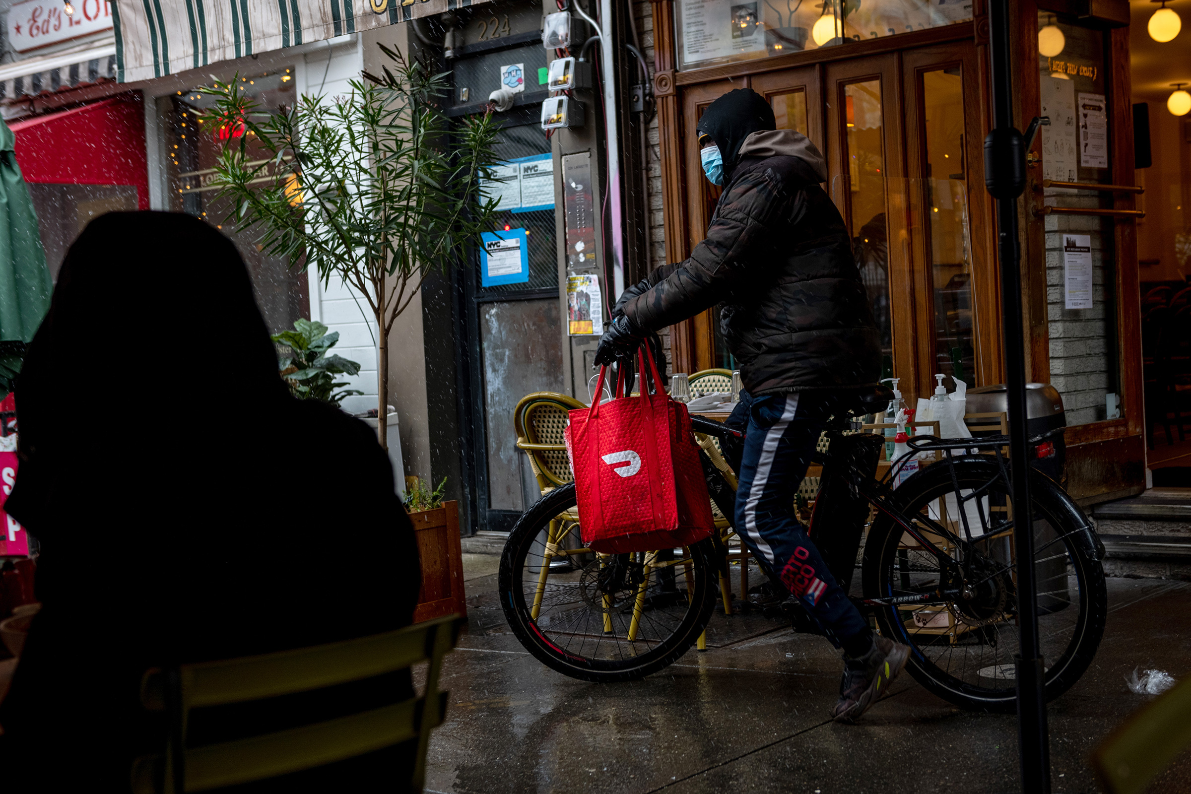 A DoorDash delivery driver riding a bicycle picks up food from a restaurant in New York City
