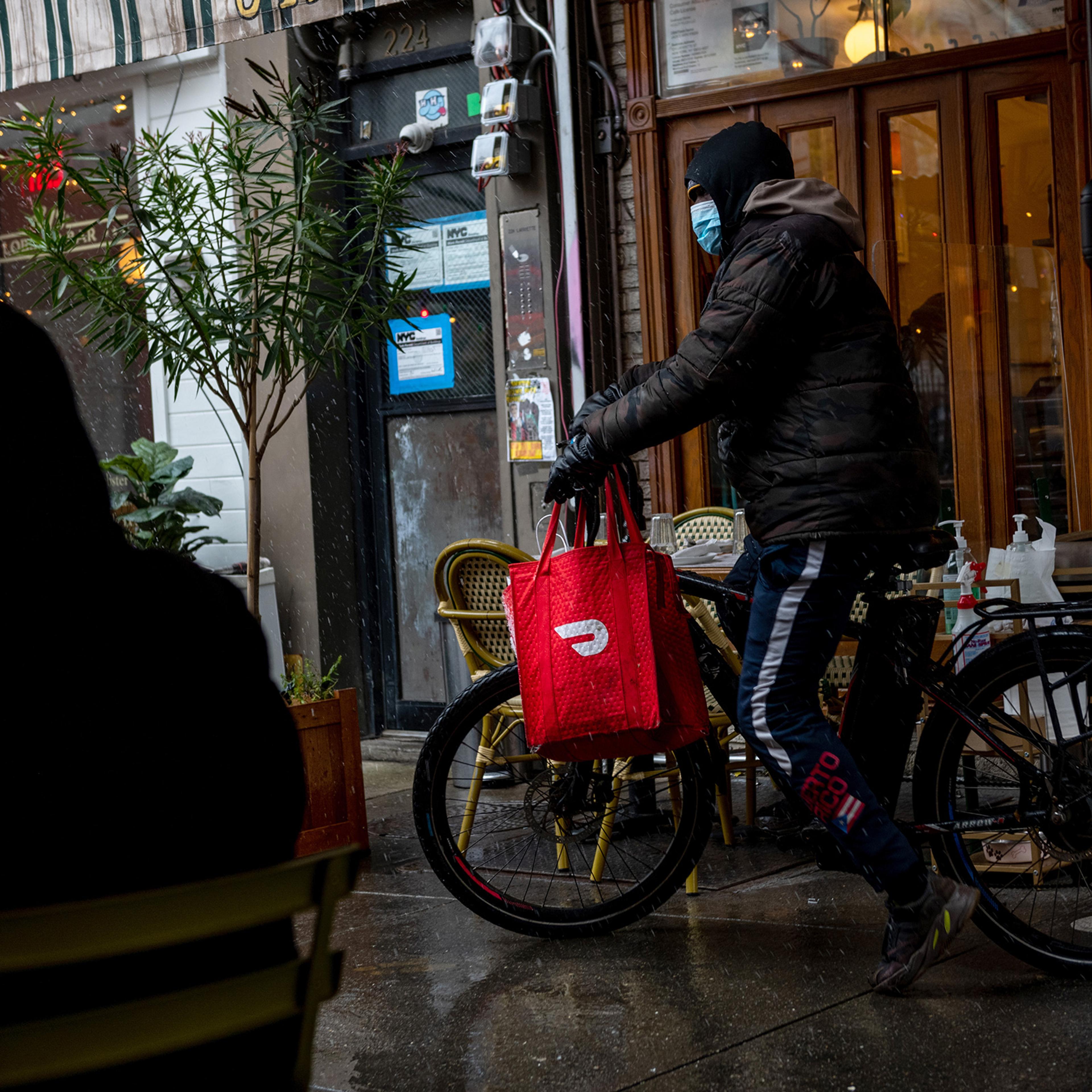 A DoorDash delivery driver riding a bicycle picks up food from a restaurant in New York City