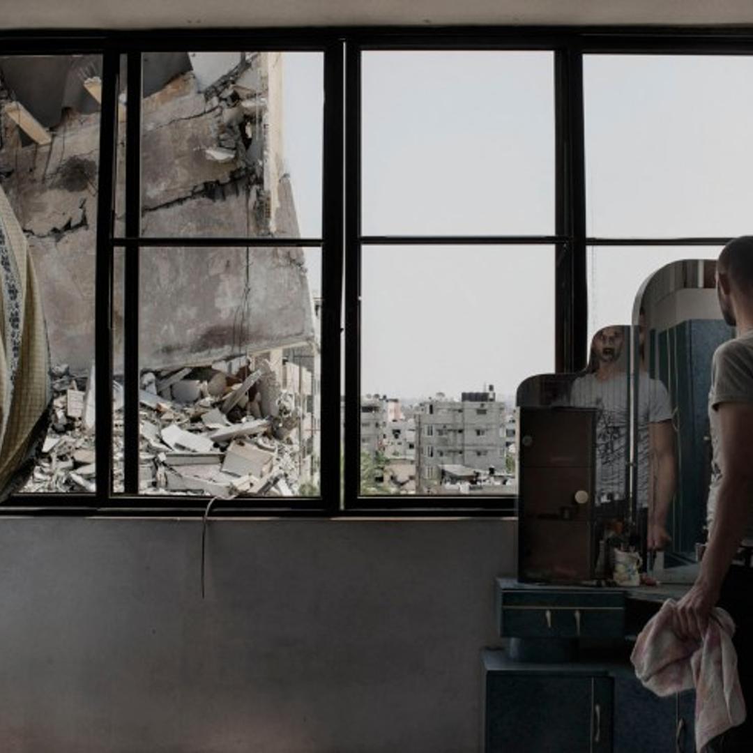 A Palestinian man looks through the window of his house to buildings damaged by an overnight airstrike in Gaza City, July 22, 2014.