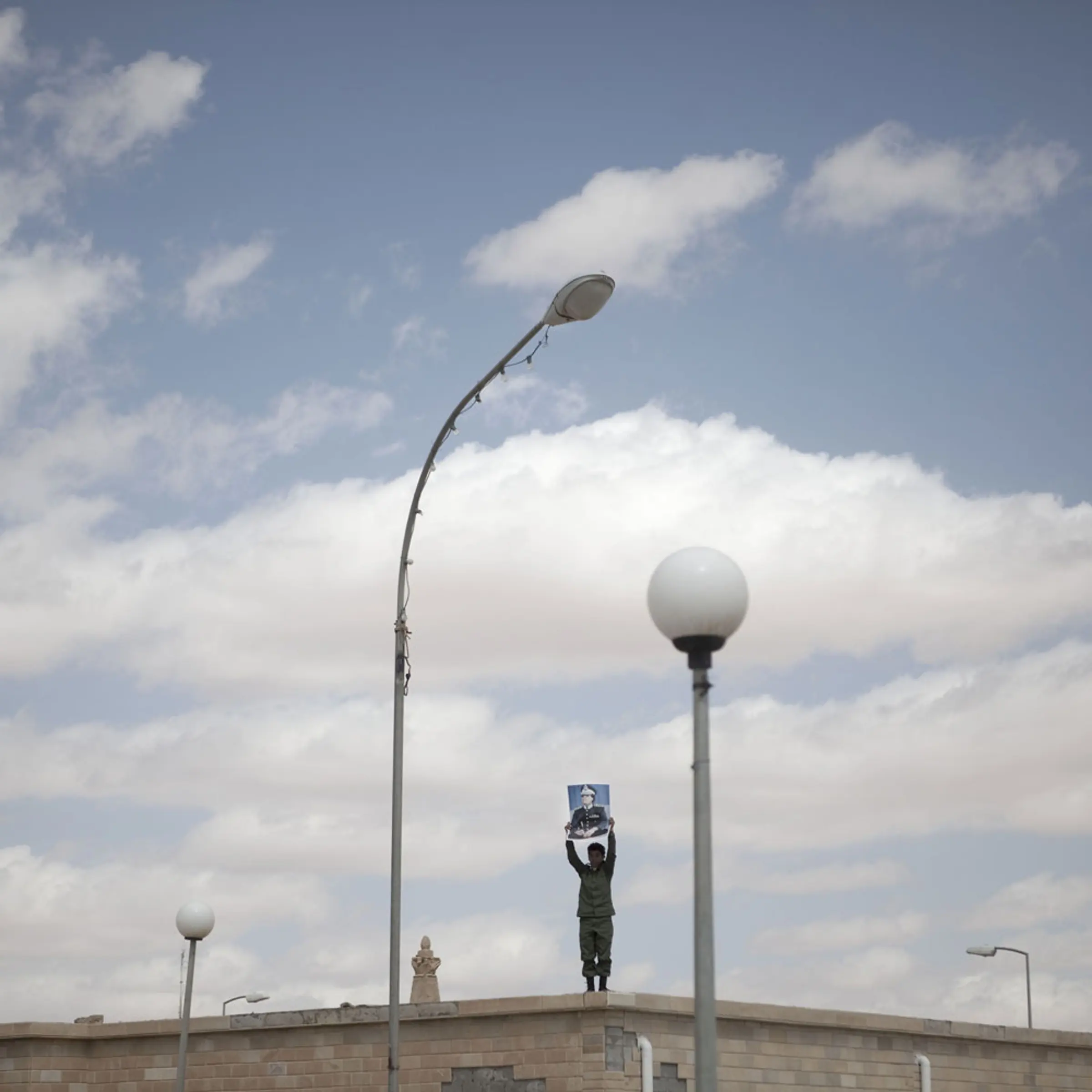 A supporter of Libyan leader Muammar Gaddafi holds a poster overlooking a demonstration in Ban-Waled, March 23, 2011.
