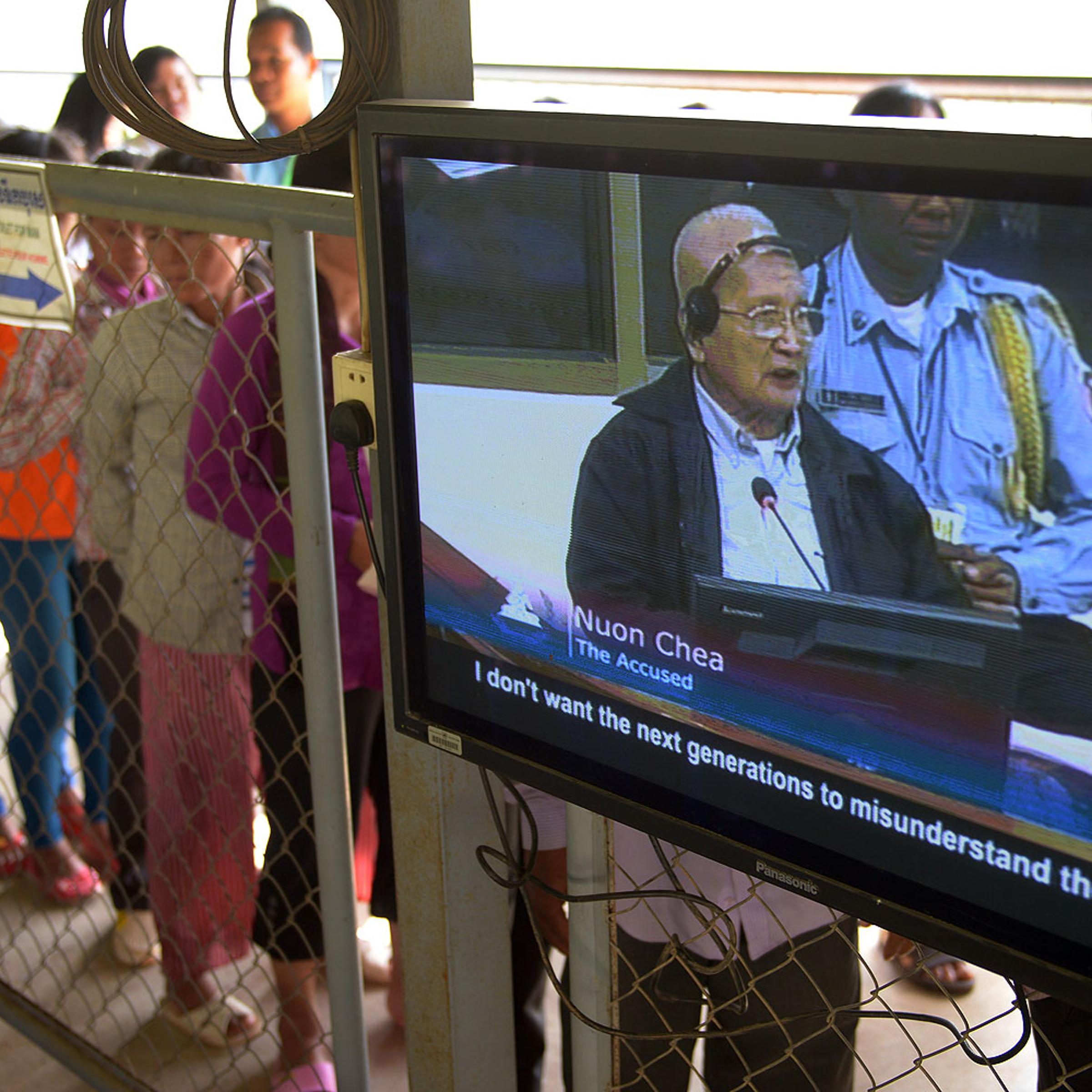 Former Cambodian Khmer Rouge leader "Brother Number Two" Nuon Chea is seen on a television screen (R) as people (L) line up to attend the trial of former Khmer Rouge leaders at the Extraordinary Chamber in the Courts of Cambodia (ECCC) in Phnom Penh in Oct. 2013