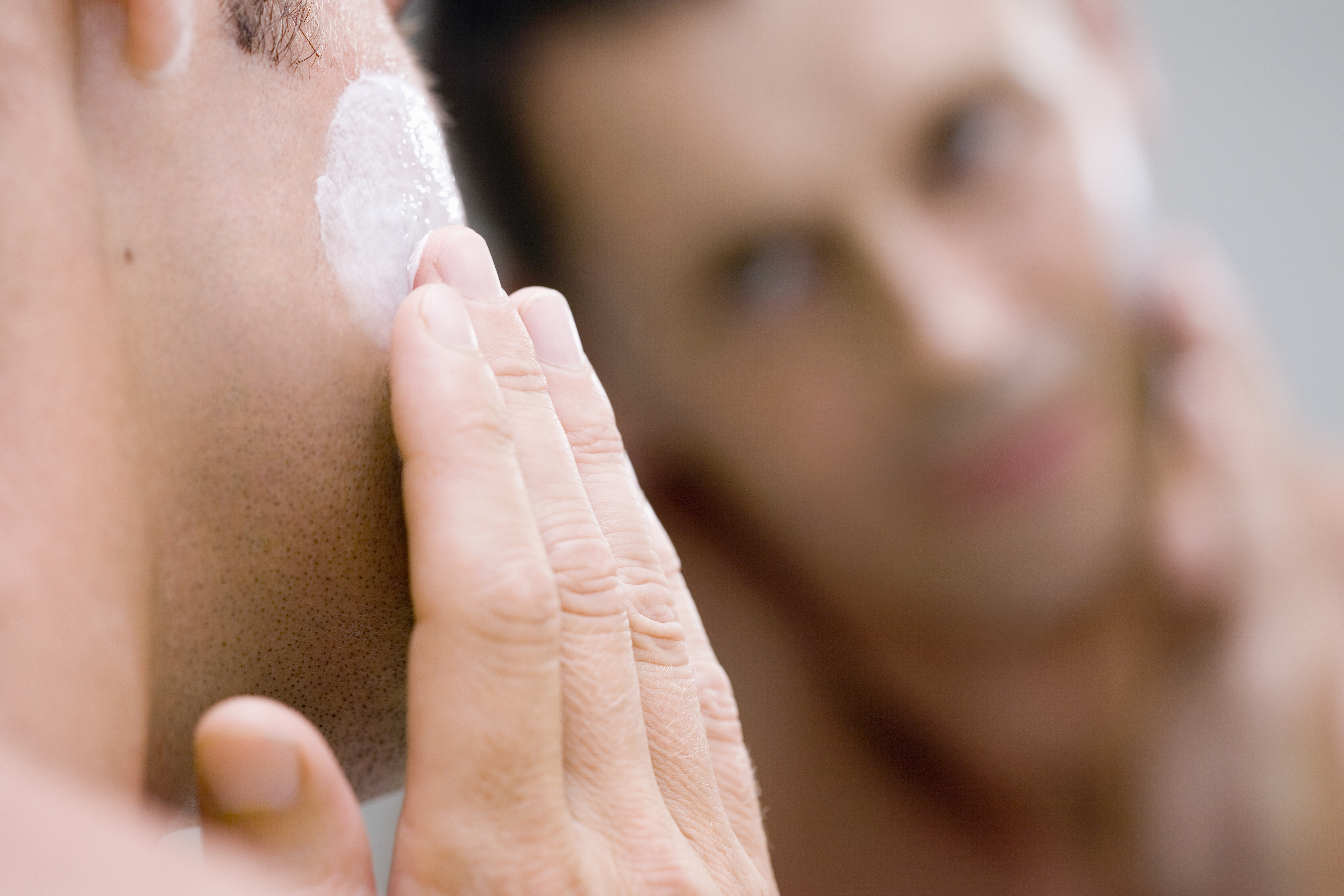 Man applying face cream in front of mirror
