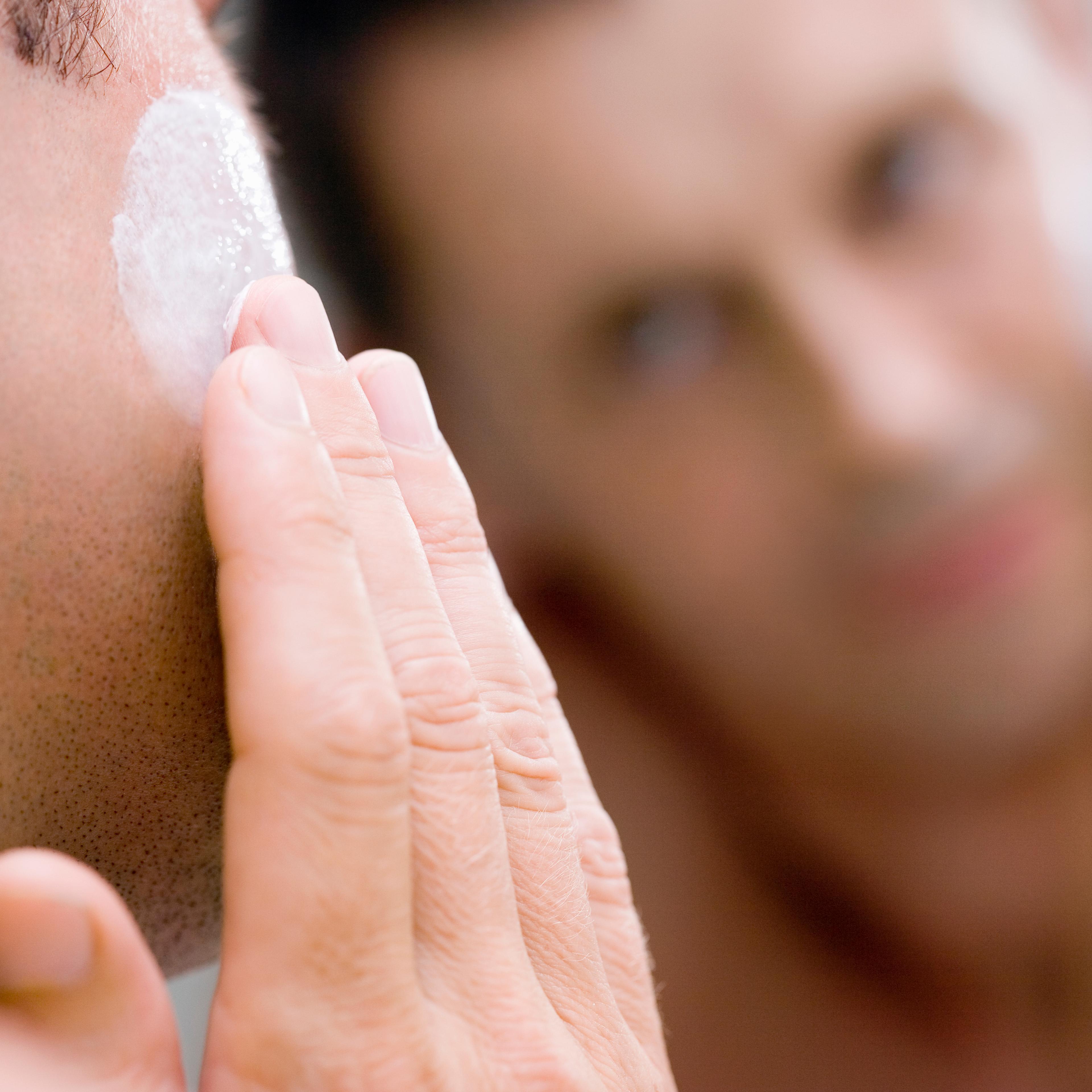 Man applying face cream in front of mirror