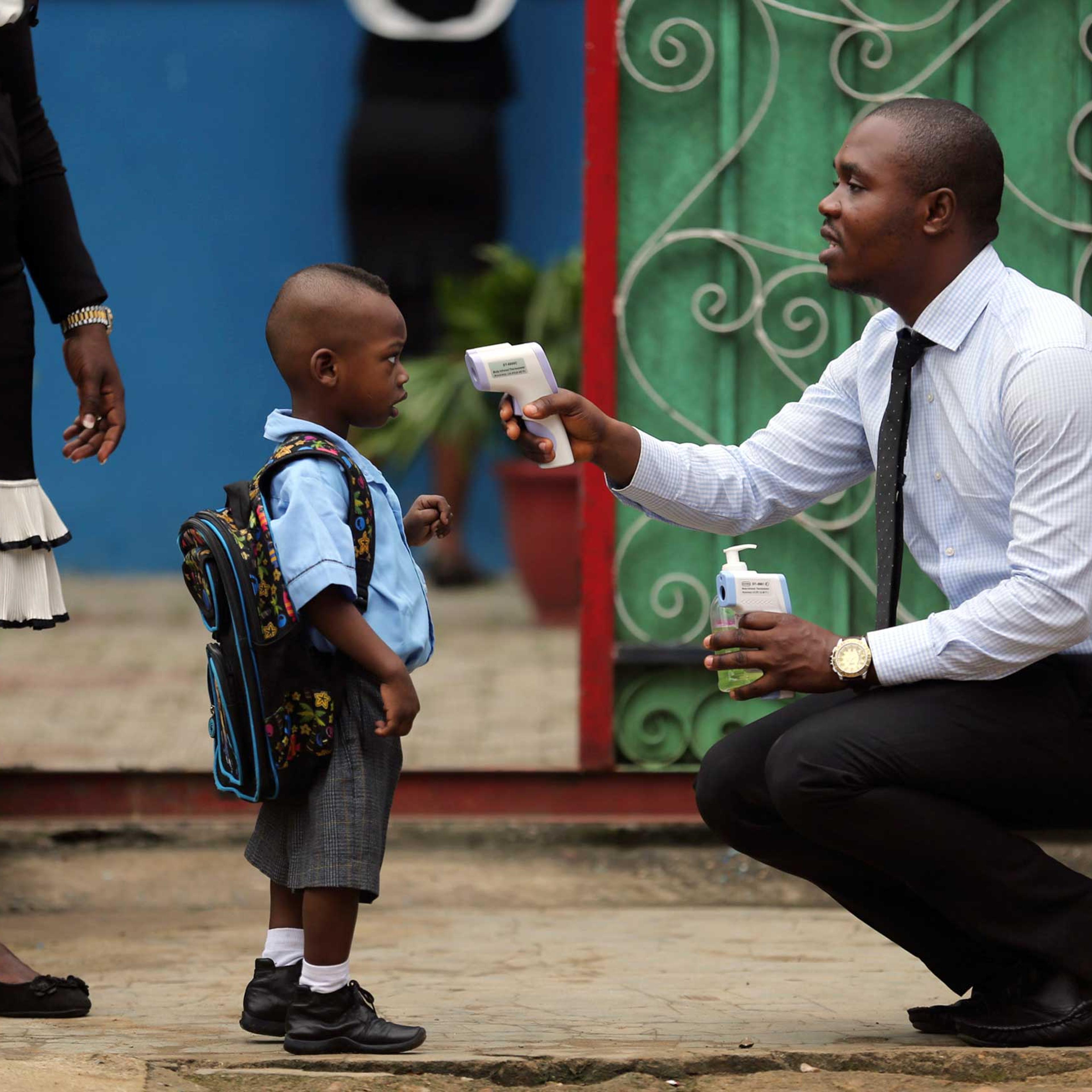 A school official takes a pupil's temperature using an infrared digital laser thermometer in front of the school premises, at the resumption of private schools, in Lagos