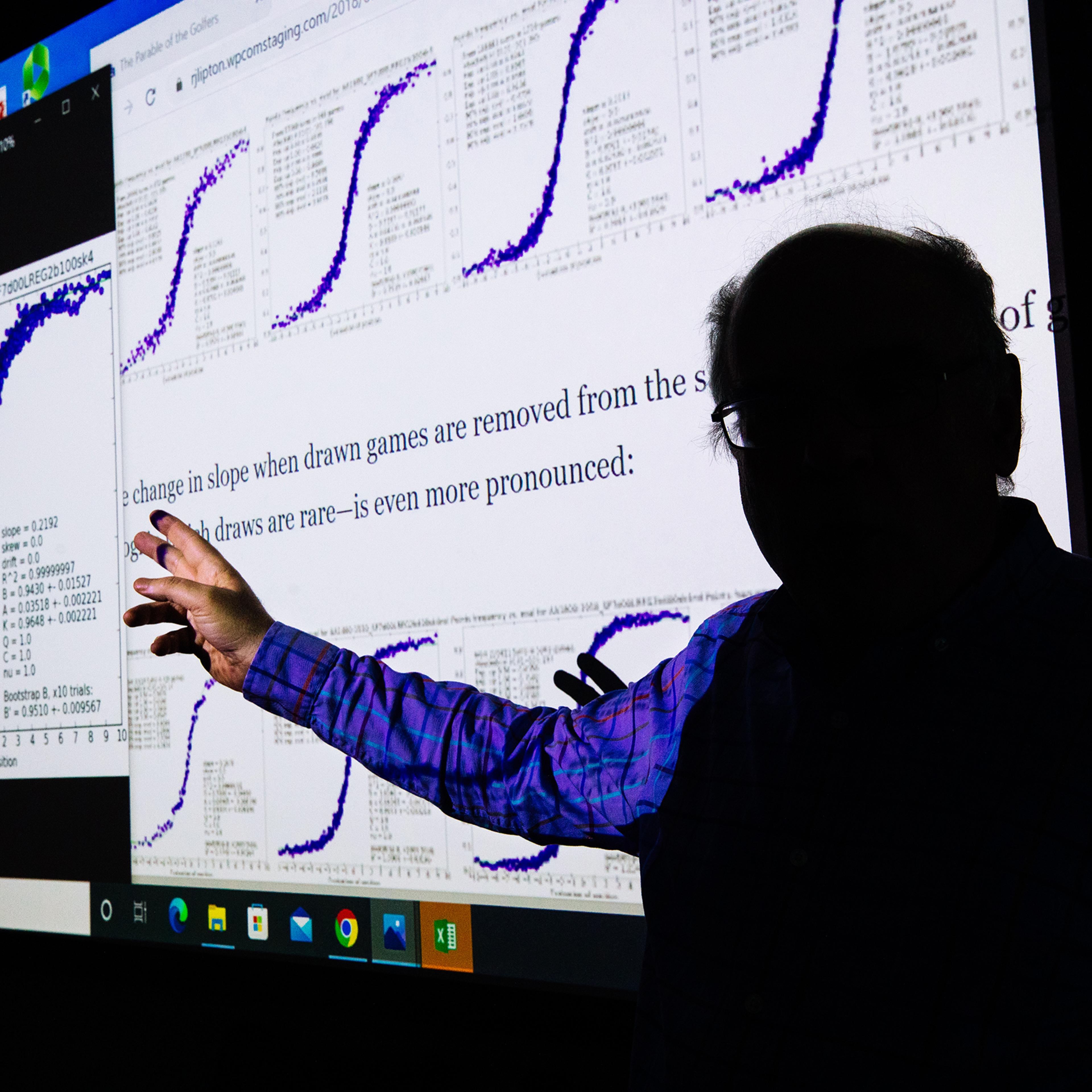 Professor Kenneth Regan inside a classroom at the University at Buffalo School of Engineering and Applied Sciences, where he teaches computer science, on Oct. 29. Behind Regan on the screen is an article he wrote about making the chess cheating test fair across players of all ratings.