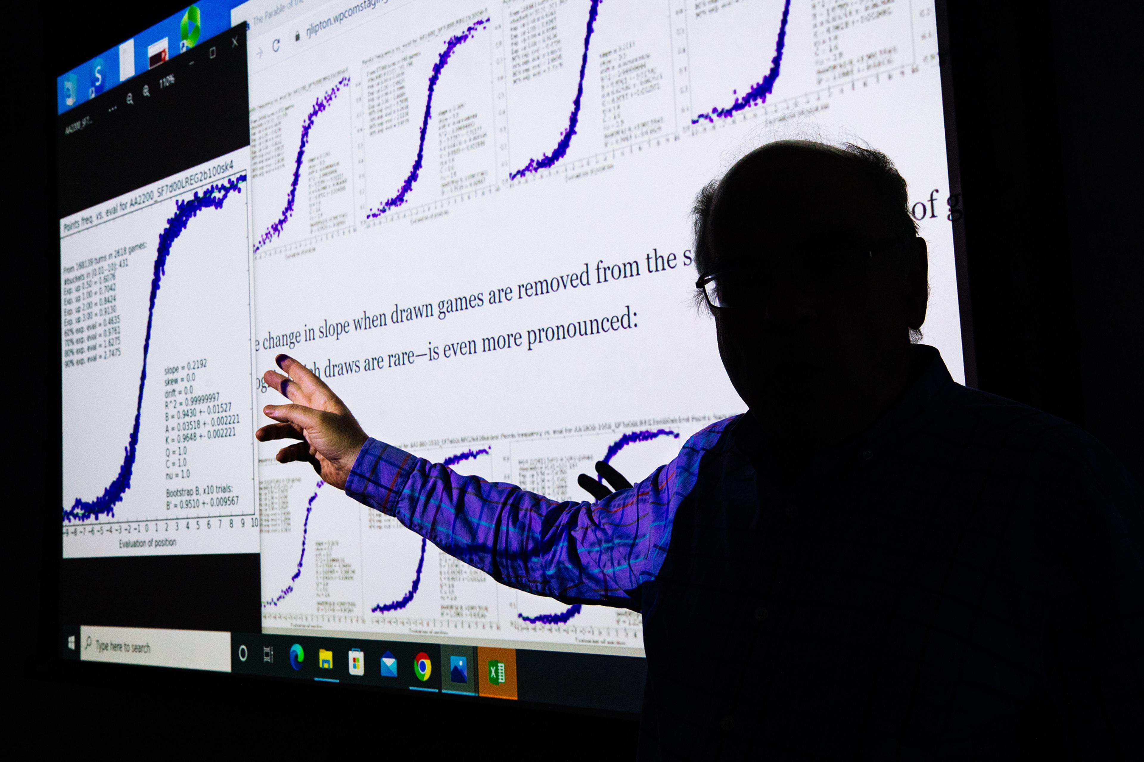 Professor Kenneth Regan inside a classroom at the University at Buffalo School of Engineering and Applied Sciences, where he teaches computer science, on Oct. 29. Behind Regan on the screen is an article he wrote about making the chess cheating test fair across players of all ratings.
