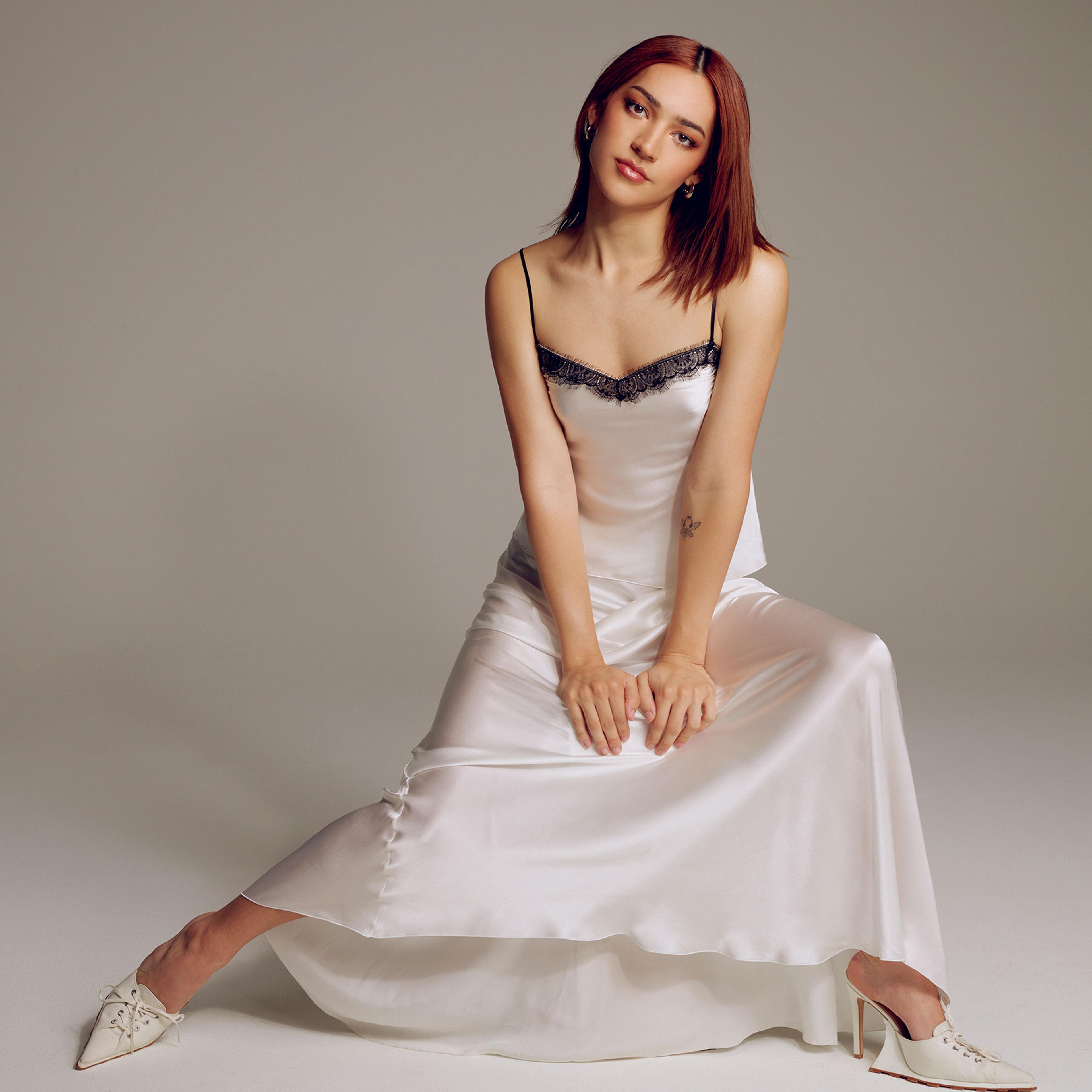Miss Benny sits and poses for a portrait in a white silk dress with black lace trim and high heels