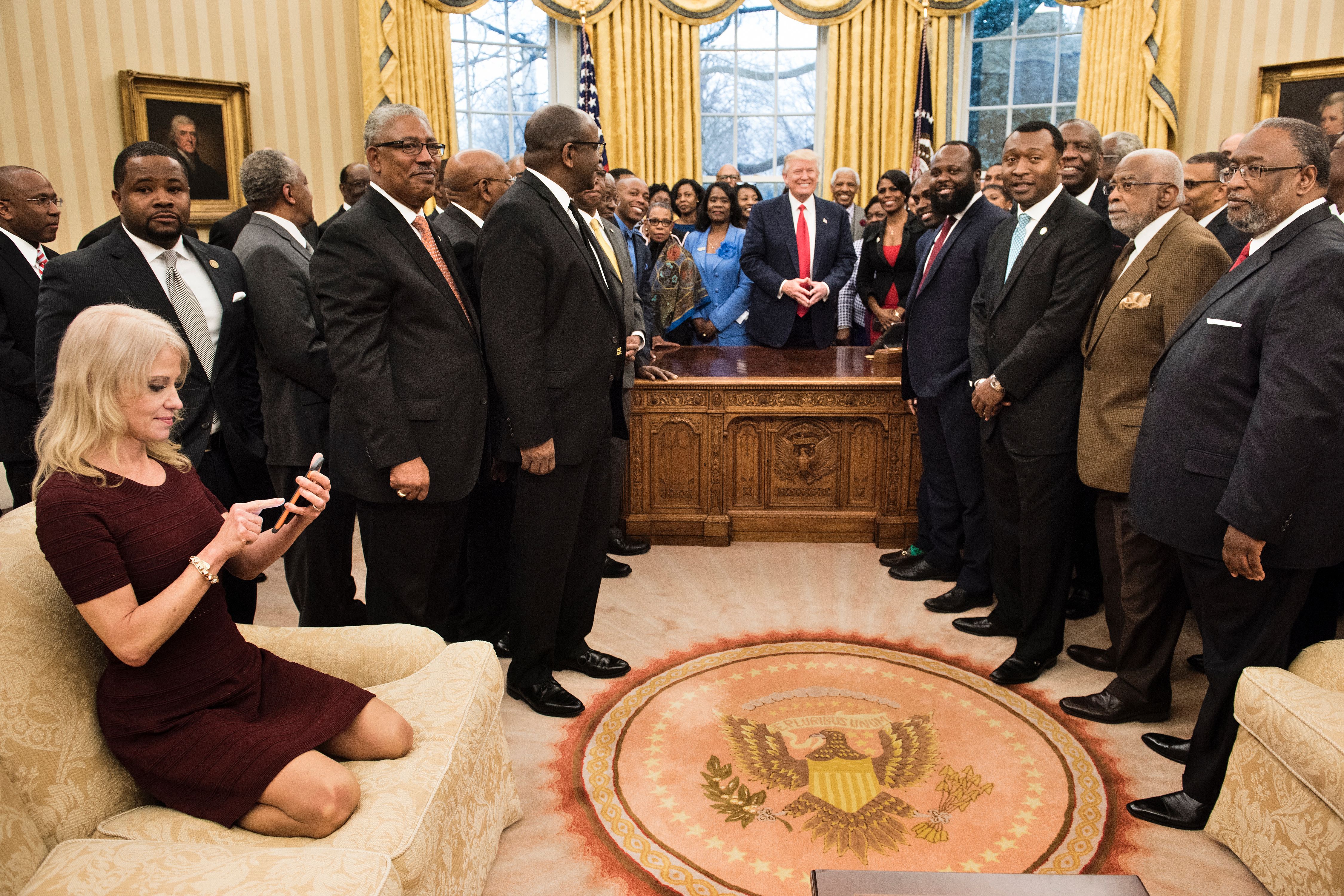 Kellyanne Conway, counselor to the President, checks her phone after taking a photo as President Trump and leaders of historically black universities and colleges pose for a group photo in the Oval Office of the White House in Washington, D.C., on Feb. 2