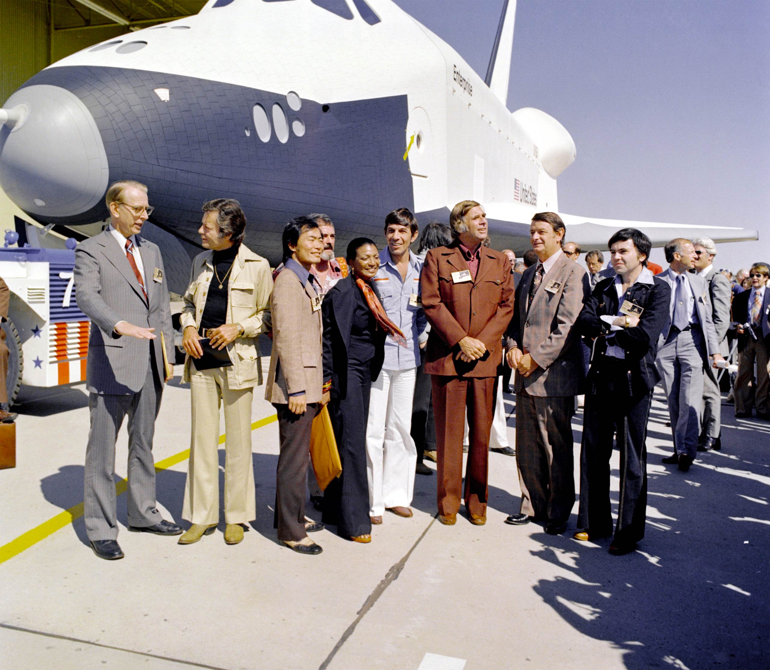 NASA's space shuttle Enterprise rolled out of the Palmdale manufacturing facilities and was greeted by NASA officials and cast members from  Star Trek in 1976. From left: NASA Administrator Dr. James D. Fletcher; DeForest Kelley, who portrayed Dr. "Bones" McCoy on the series; George Takei (Mr. Sulu); James Doohan (Chief Engineer Montgomery "Scotty" Scott); Nichelle Nichols (Lt. Uhura); Leonard Nimoy (Mr. Spock); series creator Gene Roddenberry; an unnamed NASA official; and, Walter Koenig (Ensign Pavel Chekov).