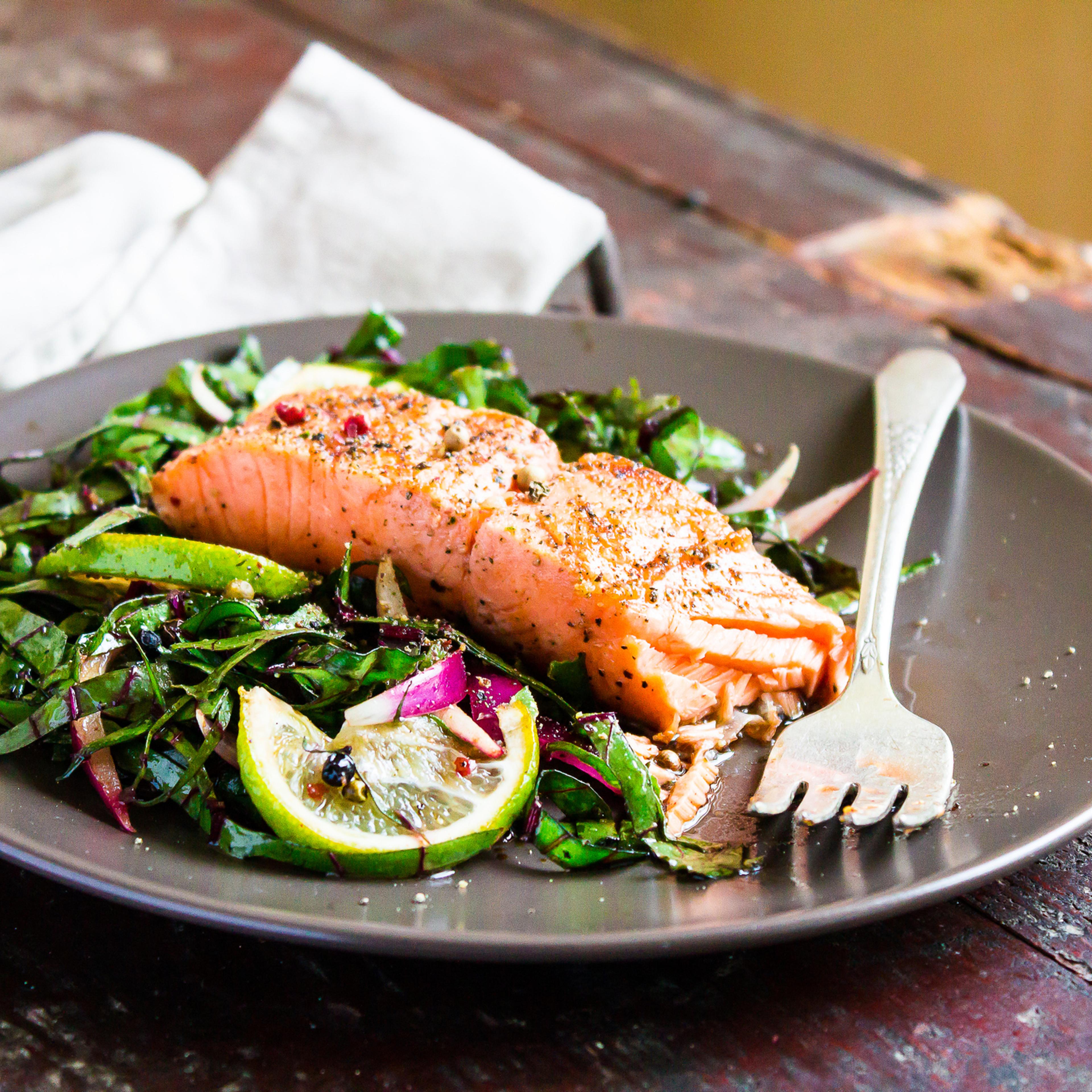 Plate of salmon fillet steak roasted with spices served with fresh salad with lime fruit and peppercorns on a wooden table, selective focus. Picnic fool. Healthy and organic food concept. Easter food.