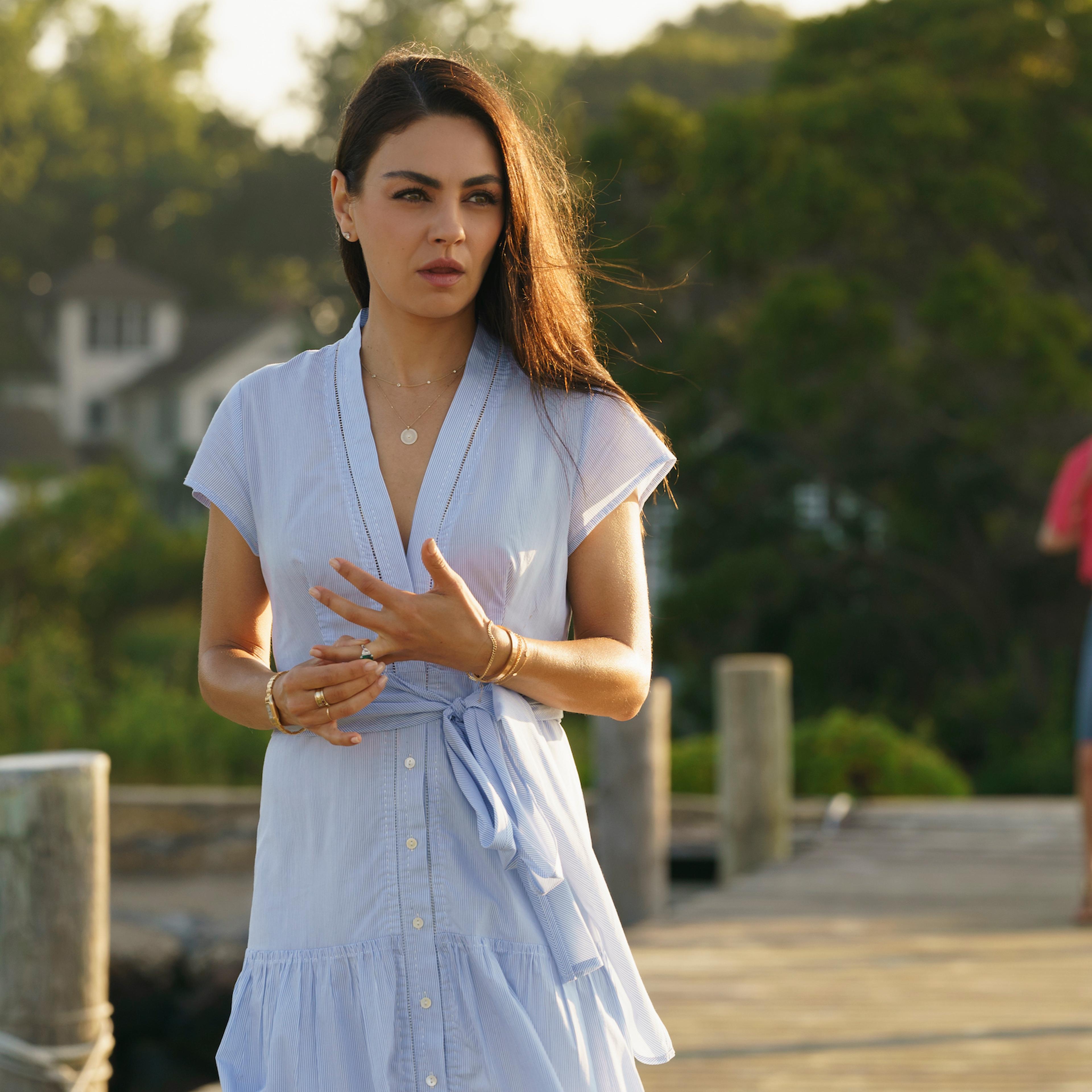 Ani fingers her engagement ring on the pier, pondering in a light blue dress