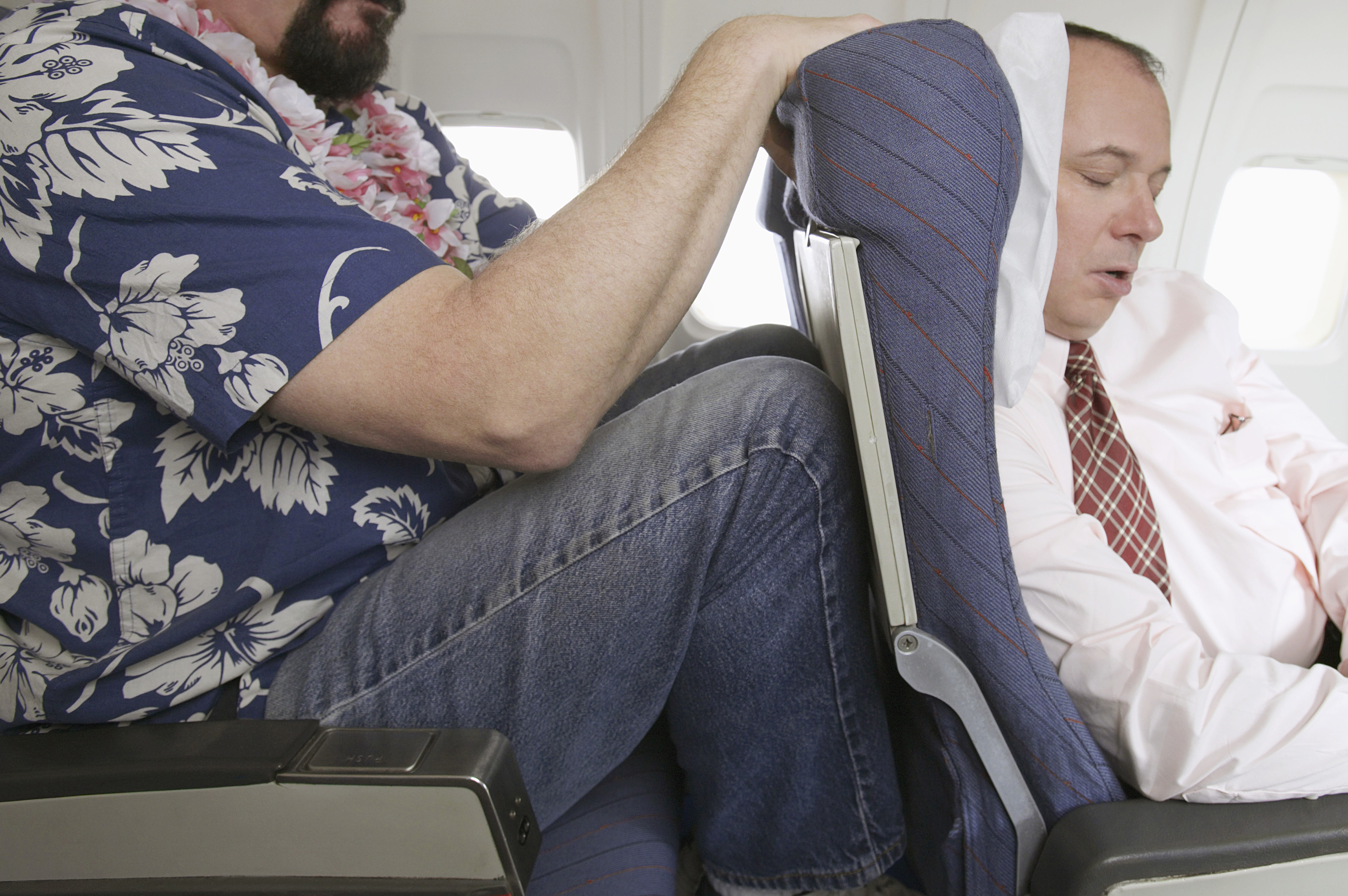 Passenger With His Knees Against a Sleeping Businessman's Chair on an Aeroplane