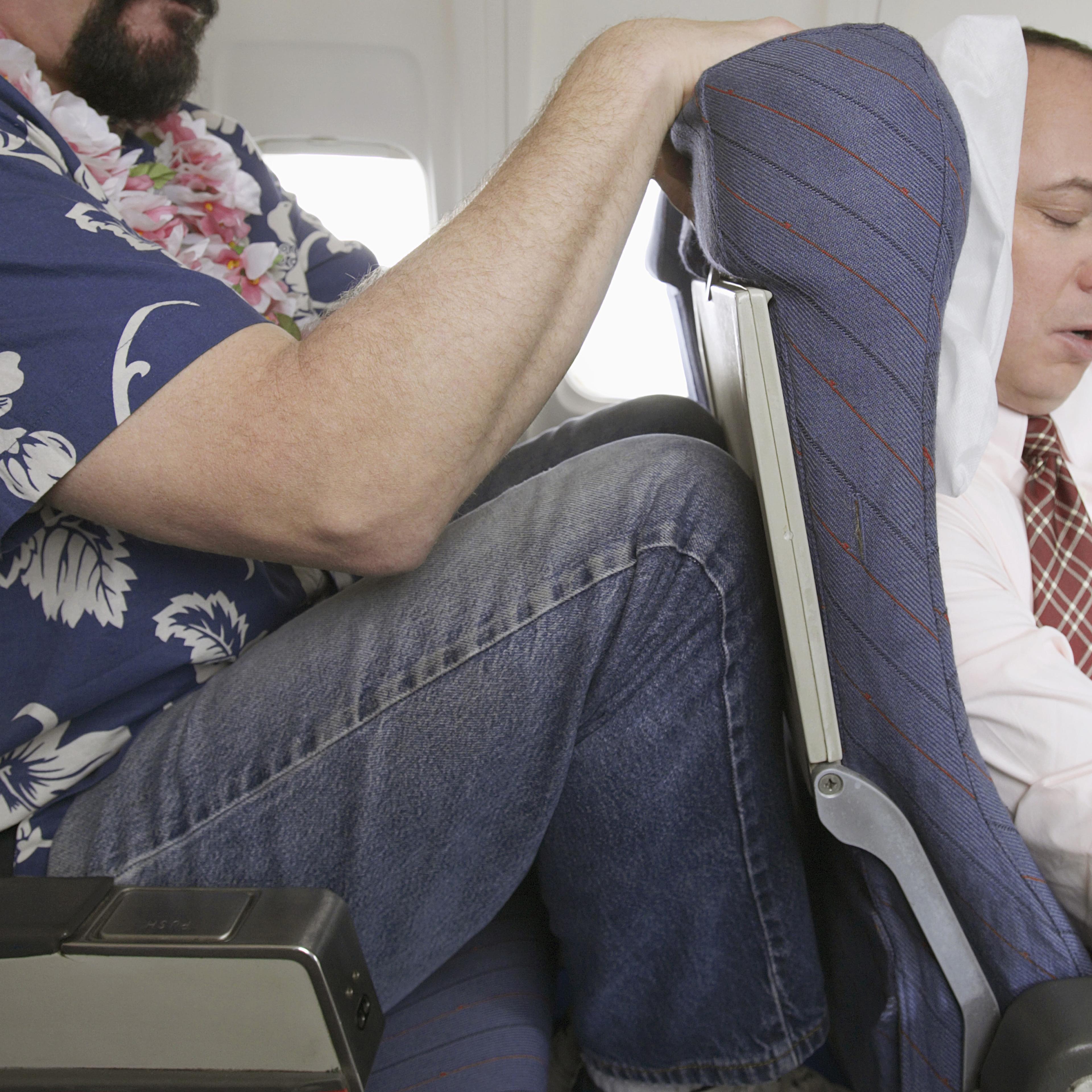 Passenger With His Knees Against a Sleeping Businessman's Chair on an Aeroplane