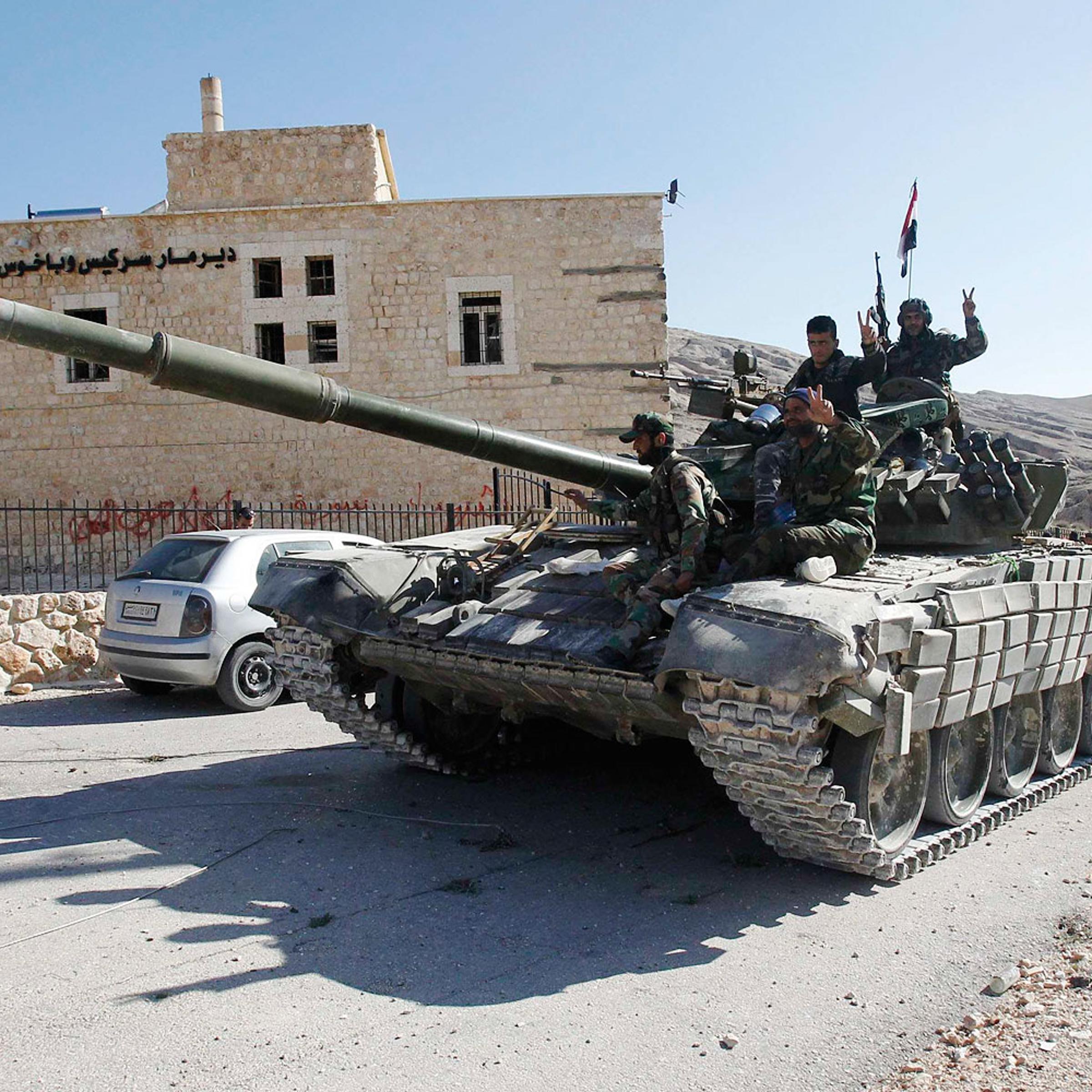 Soldiers loyal to Syria's President Bashar al-Assad gesture from their tank, as they pass Mar Bacchus Sarkis monastery, in Maloula village, northeast of Damascus, after taking control of the village from rebel fighters April 14, 2014.