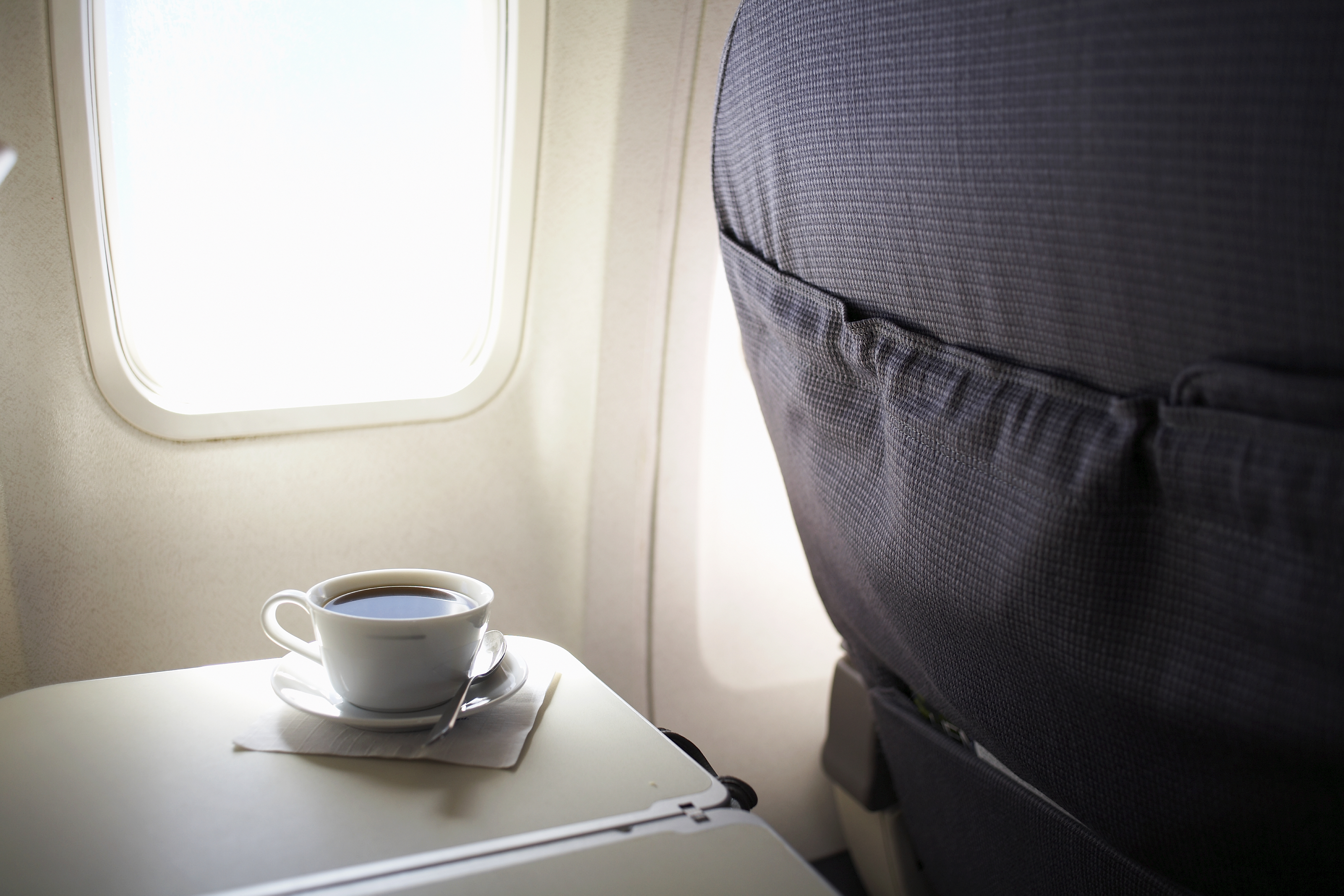 Cup of coffee on airplane tray table by window, elevated view