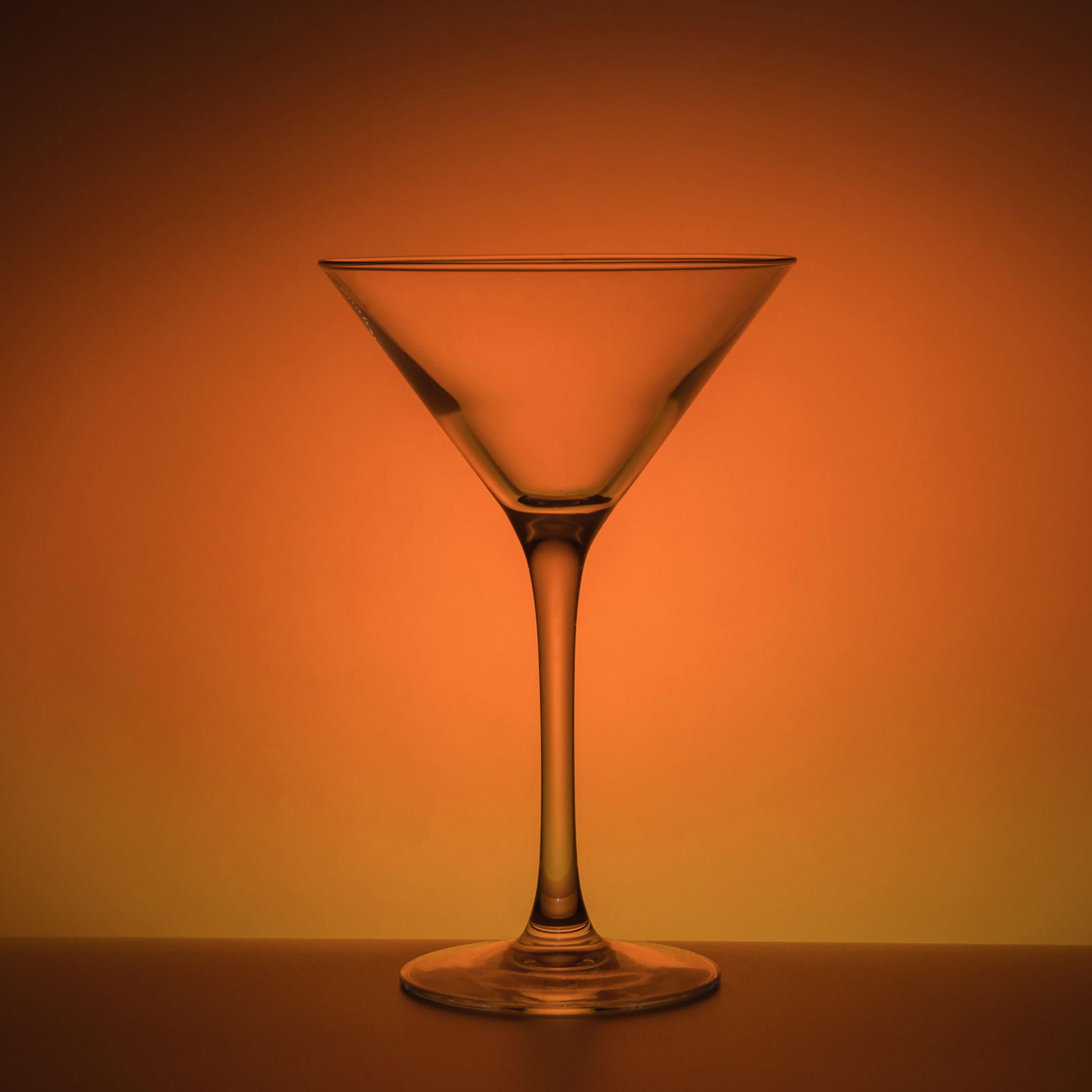 An empty transparent martini glass on a moody orange background
