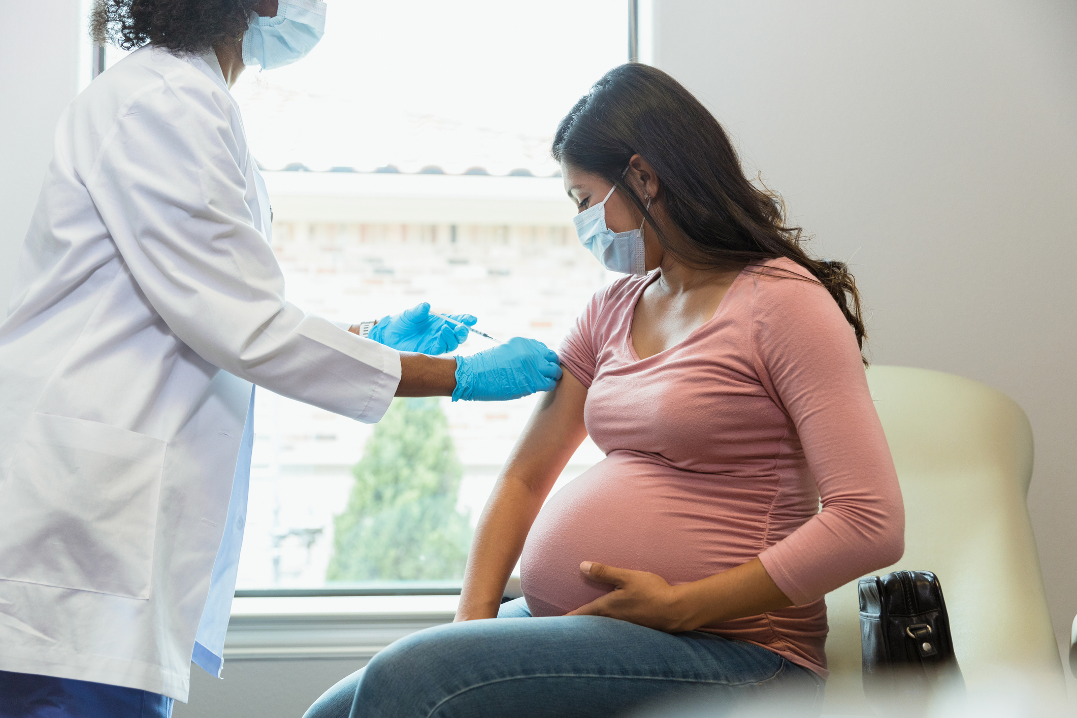 Expectant mother watches as tech gives her vaccine